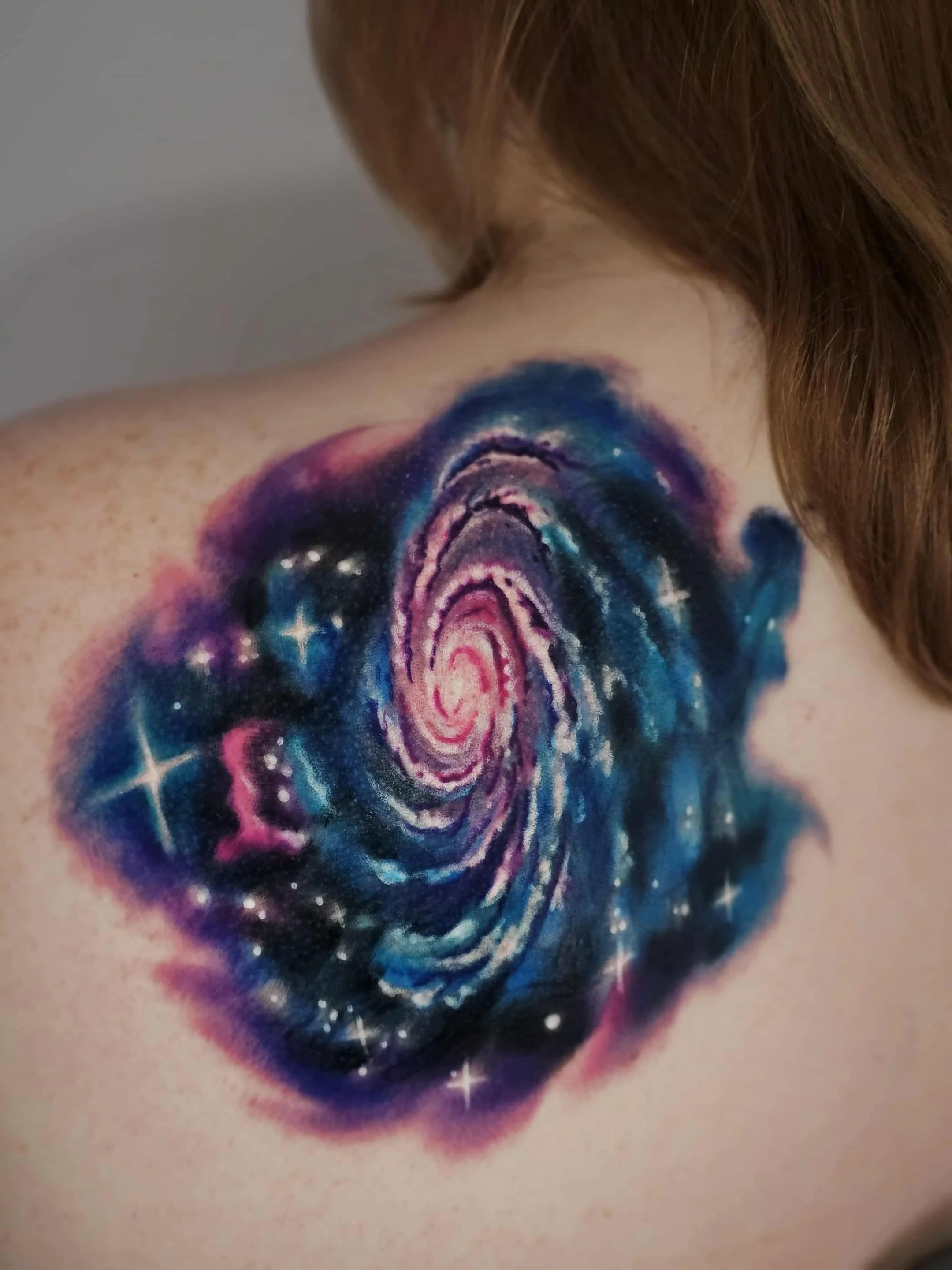Colorful galaxy-themed tattoo on person's shoulder with swirling spiral design and star-like accents.