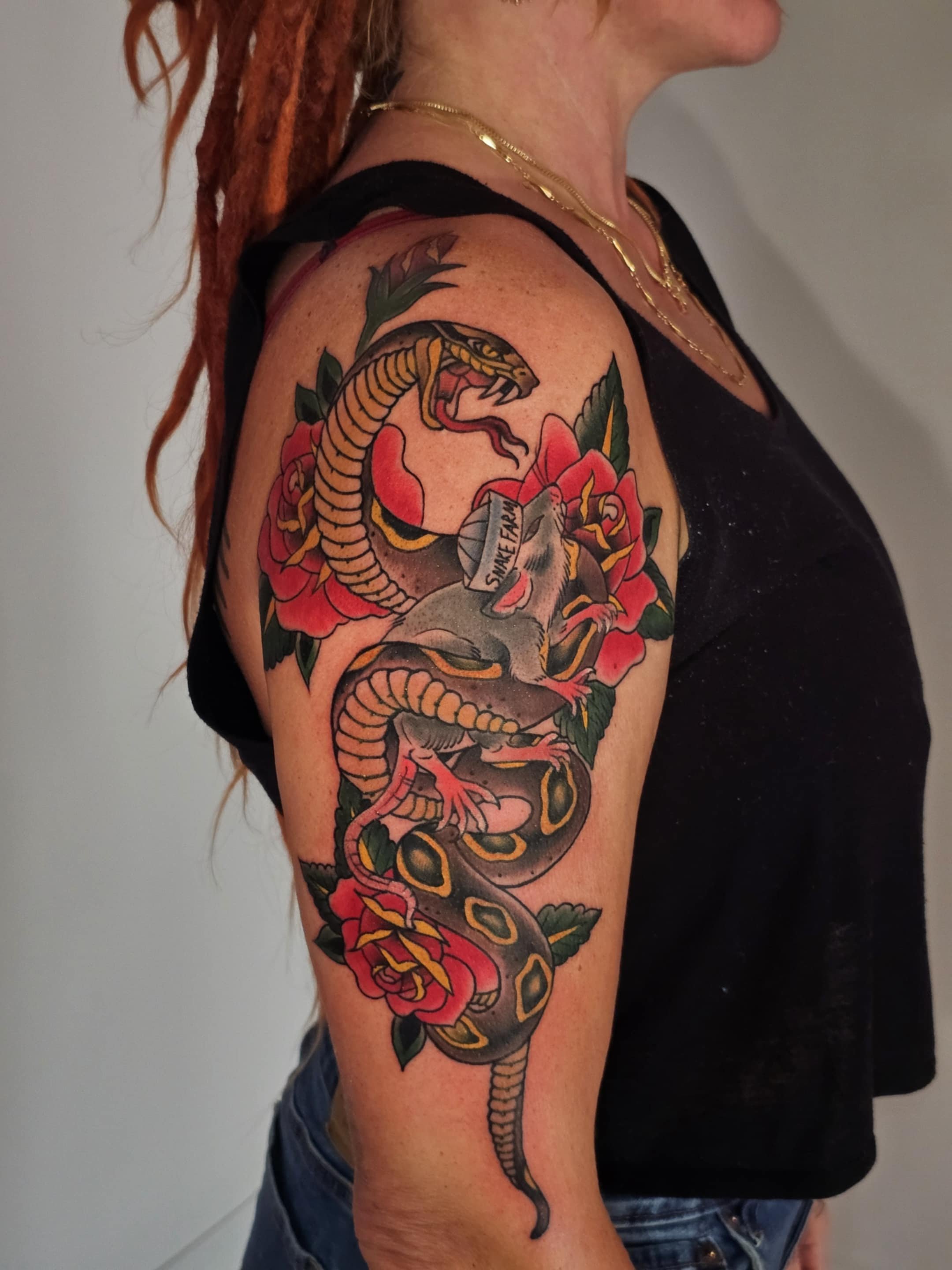 Tattoo of a snake entwined with a rat and surrounded by pink and red roses on a woman's upper arm.