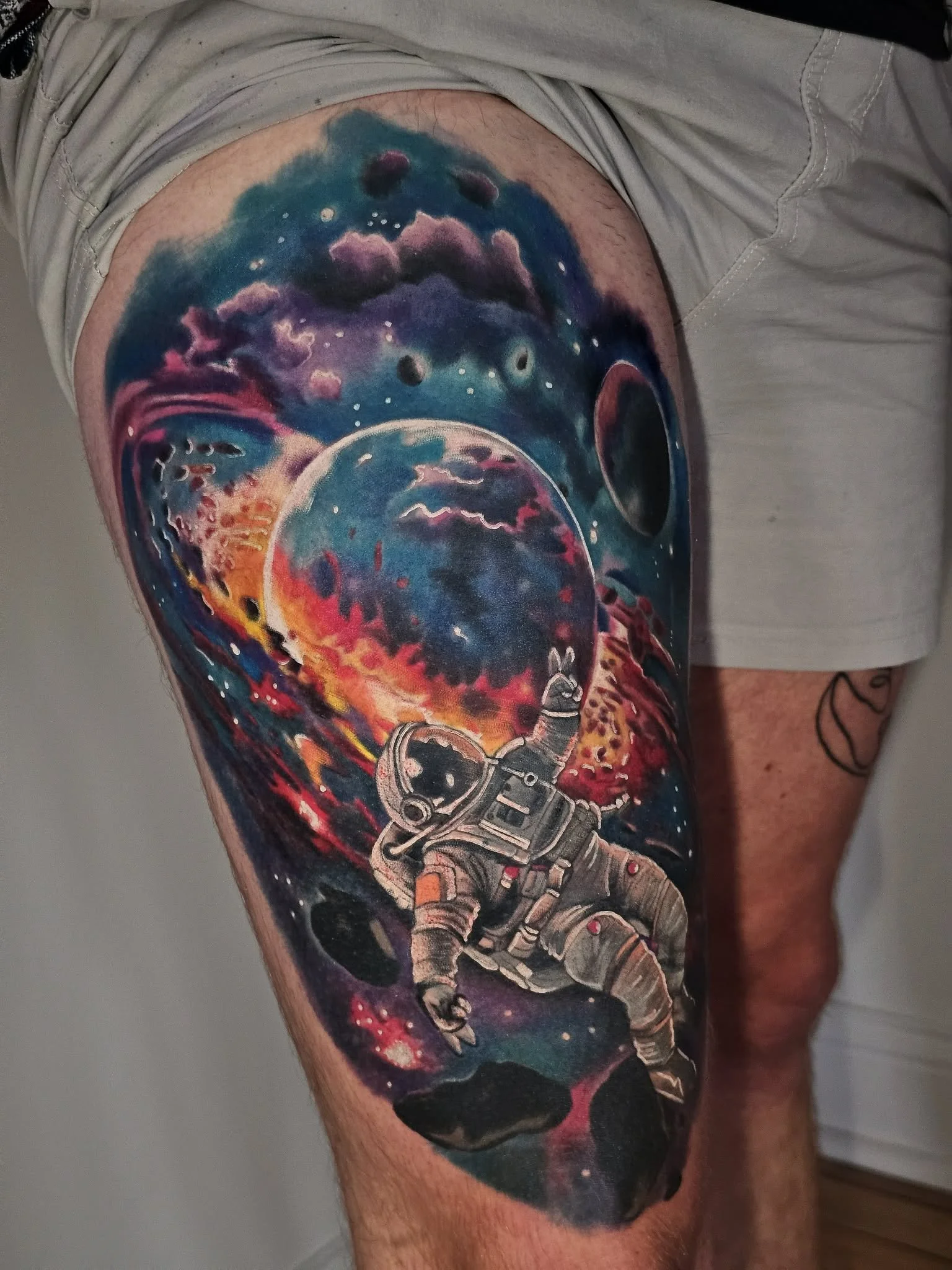 Colorful tattoo of an astronaut floating in space with planets and cosmic clouds in the background.