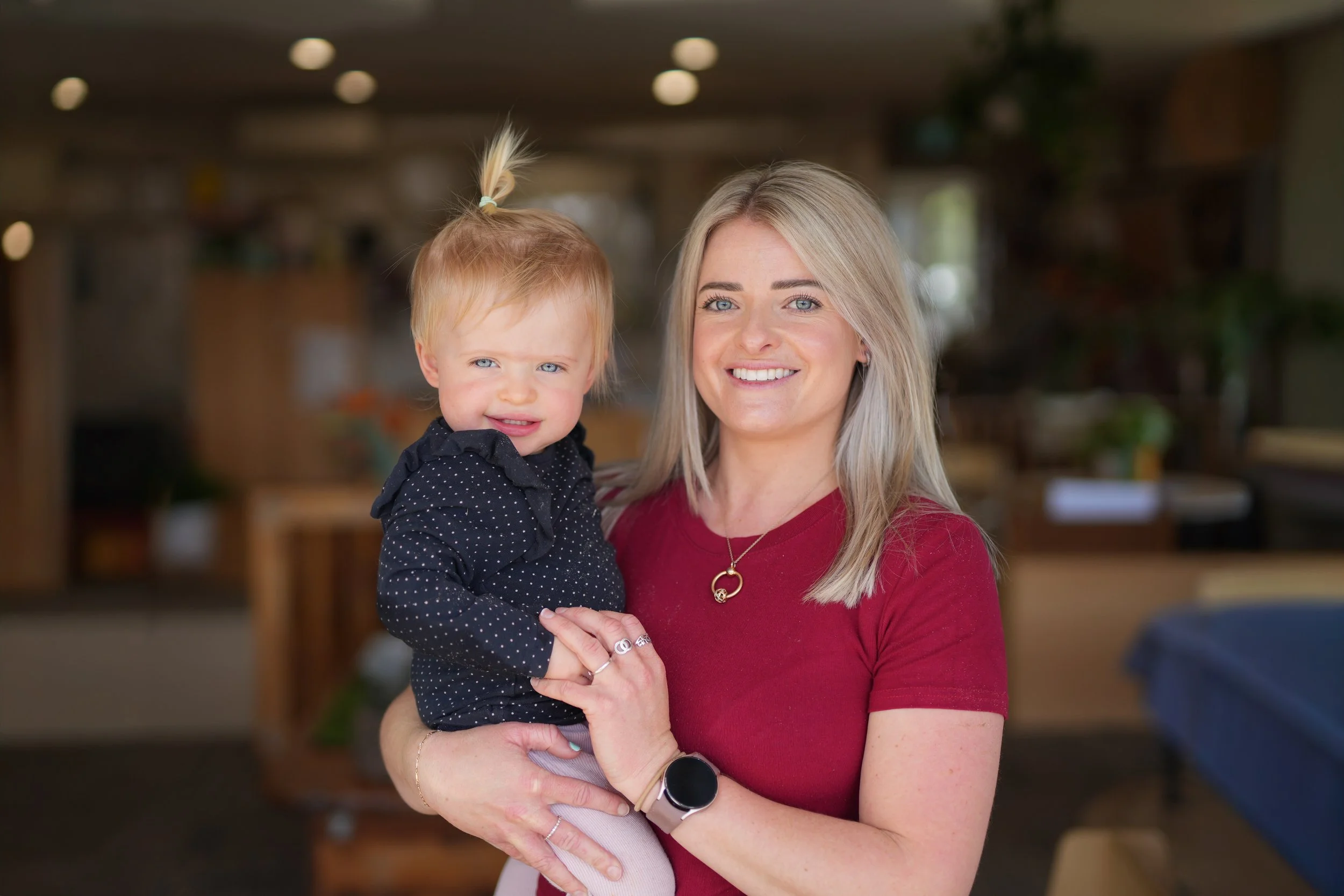 A woman holding a young girl indoors, both smiling at the camera.