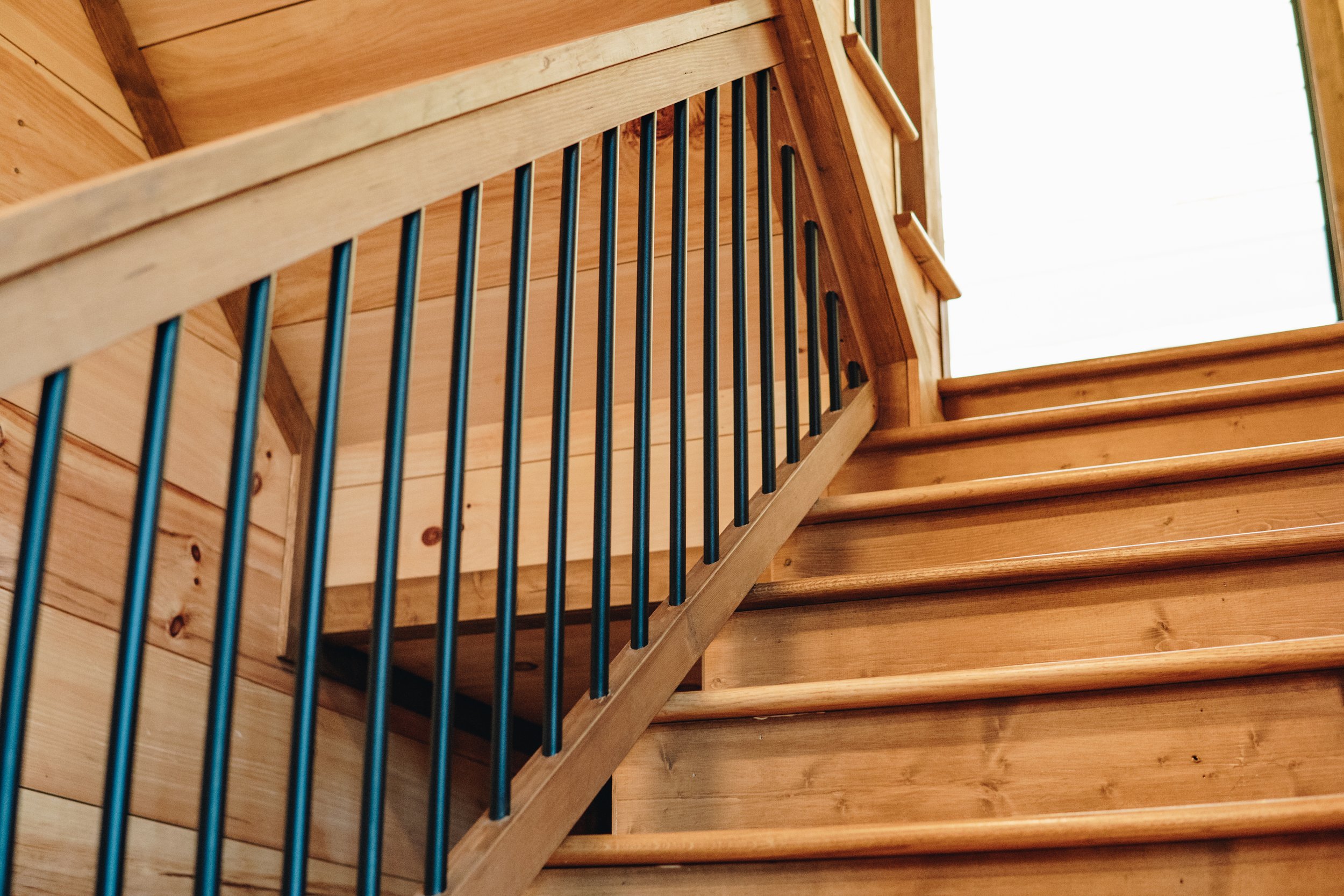 Wooden staircase with black metal handrail and wooden wall panels.