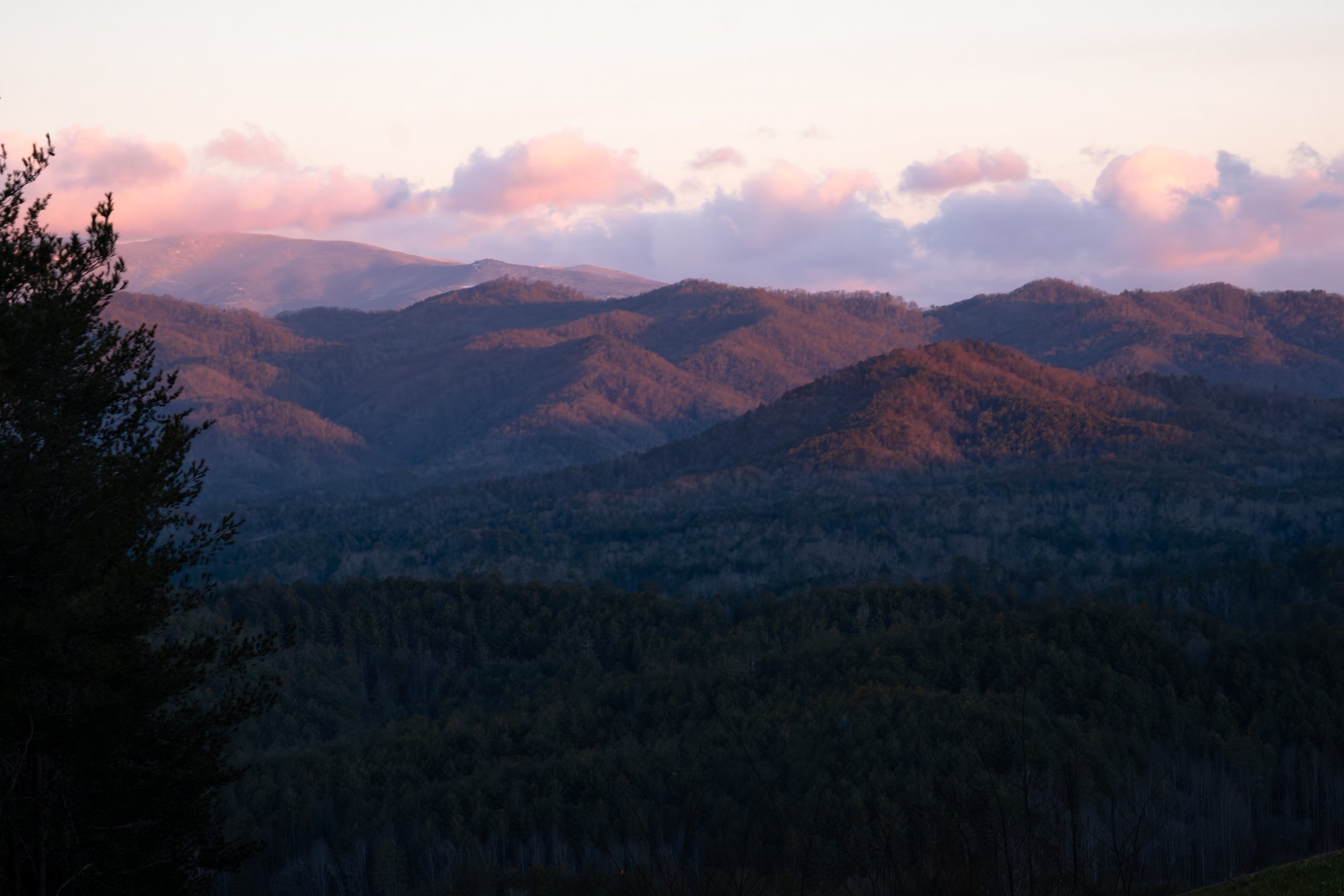 Mountain landscape with rolling hills and a sky with pink and purple clouds during sunrise or sunset.