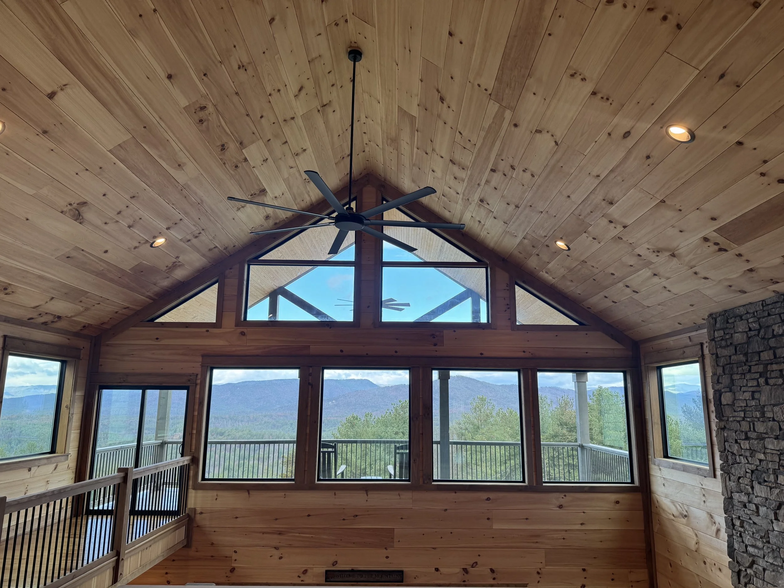 Interior of a wooden cabin with large windows, mountain view, ceiling fan, and recessed lighting.