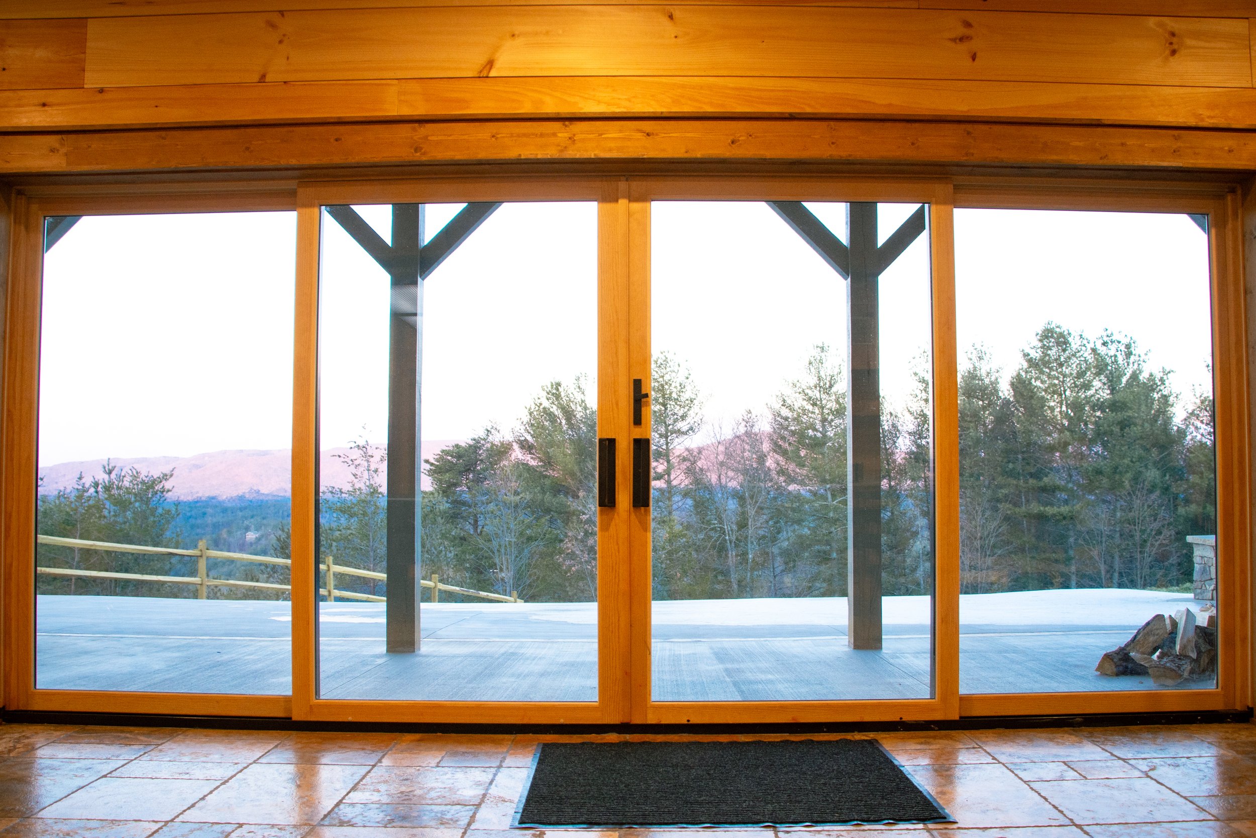 Interior view of a house showing a sliding glass door leading to a balcony with trees and distant mountains outside.