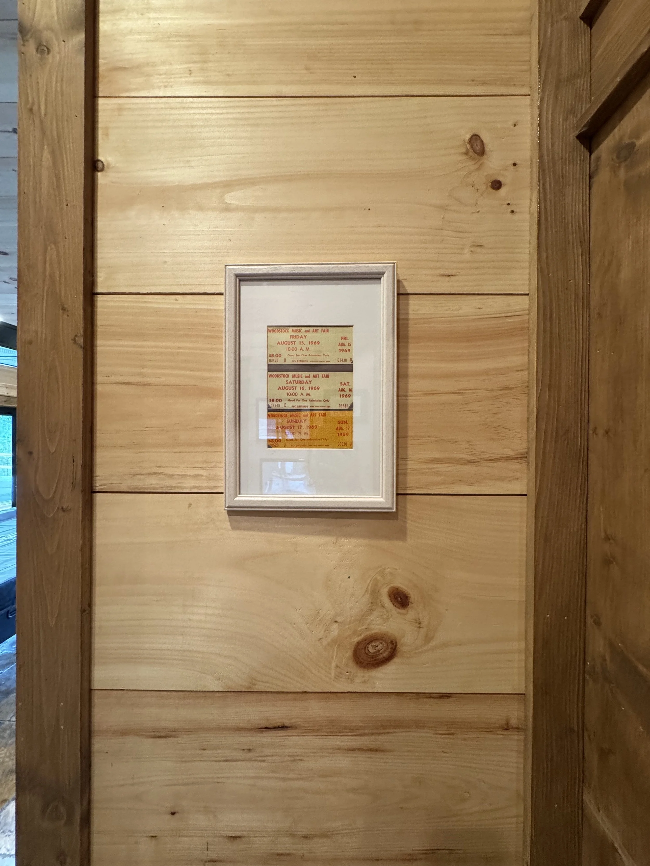 Framed ticket stubs for a Woodstock Music and Art Fair in 1969, hung on a wooden wall.