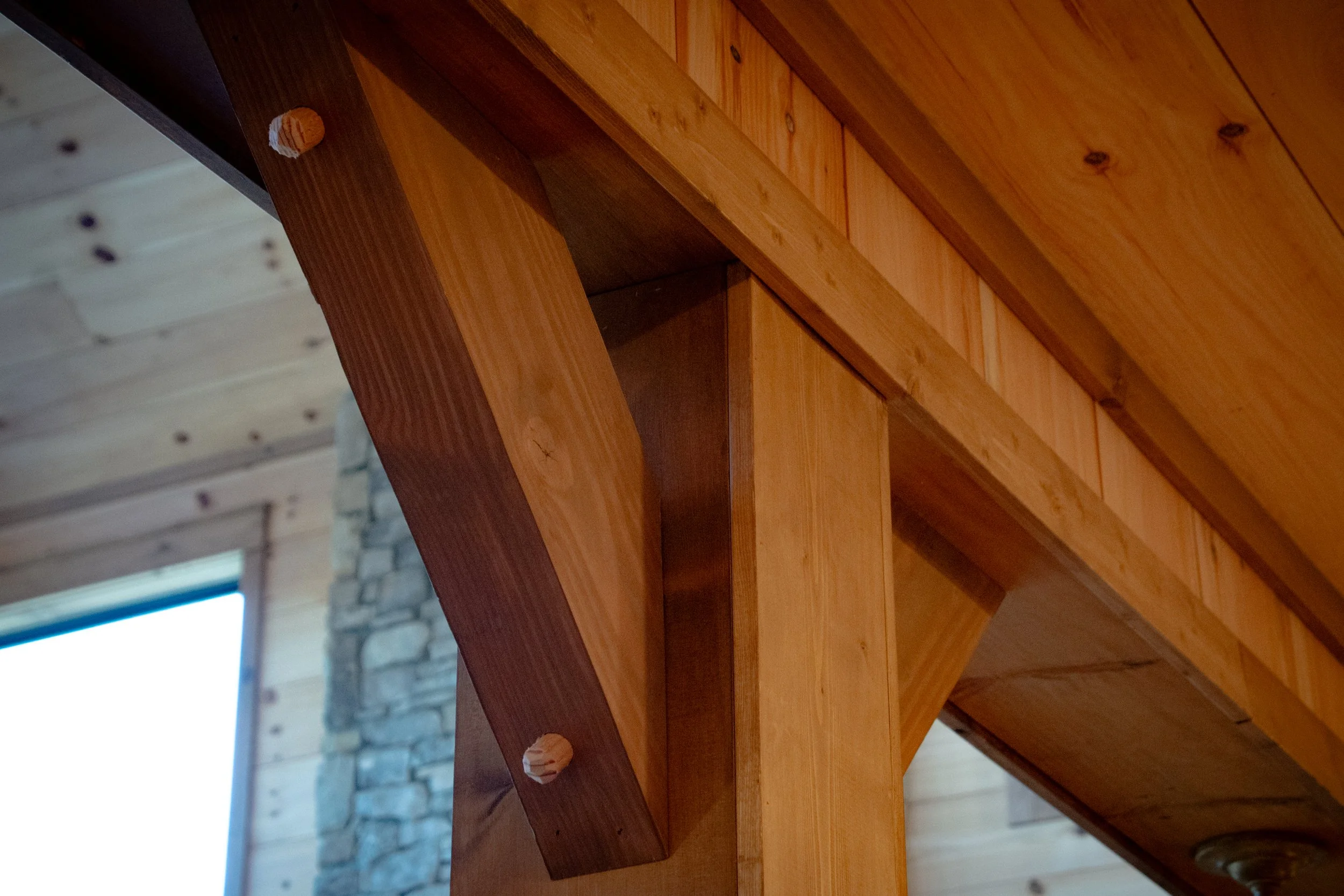 Close-up of a wooden beam and support structure inside a building with wood-paneled ceiling and stone wall in the background.