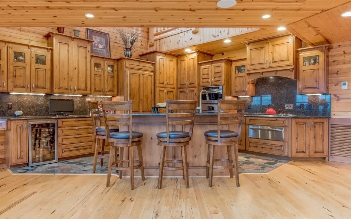 Kitchen with wooden cabinets, granite countertops, and a breakfast bar with three wooden chairs with black cushions.