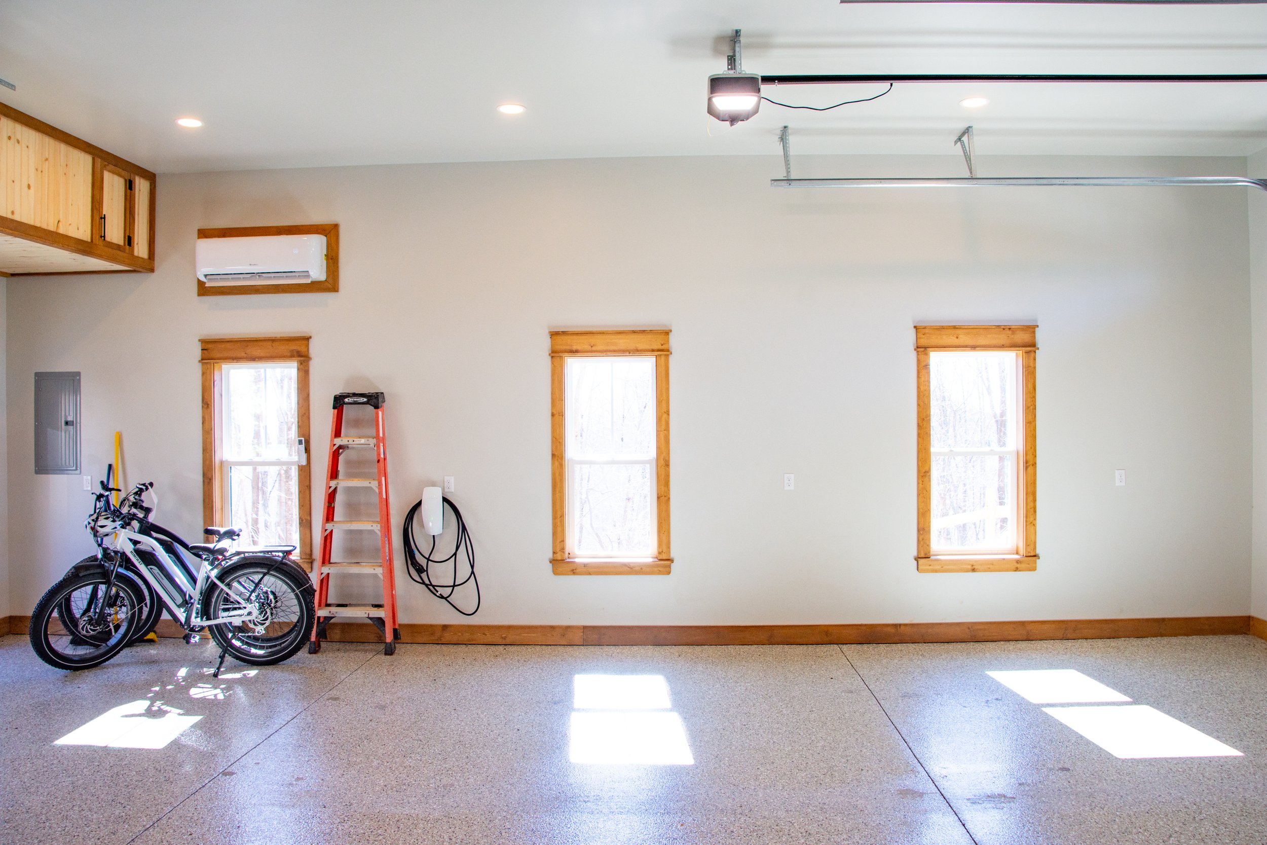 Empty garage with three windows, two bicycles, a red ladder, a hose, and a garage door opener.