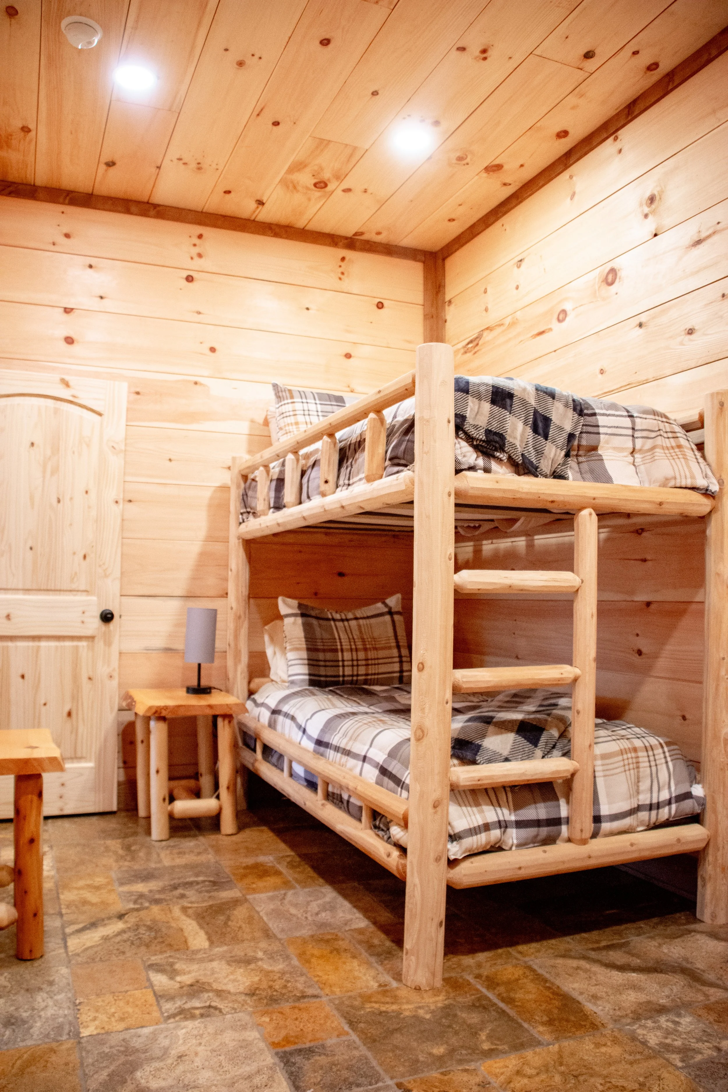Bedroom with wooden walls and a bunk bed with plaid bedding.