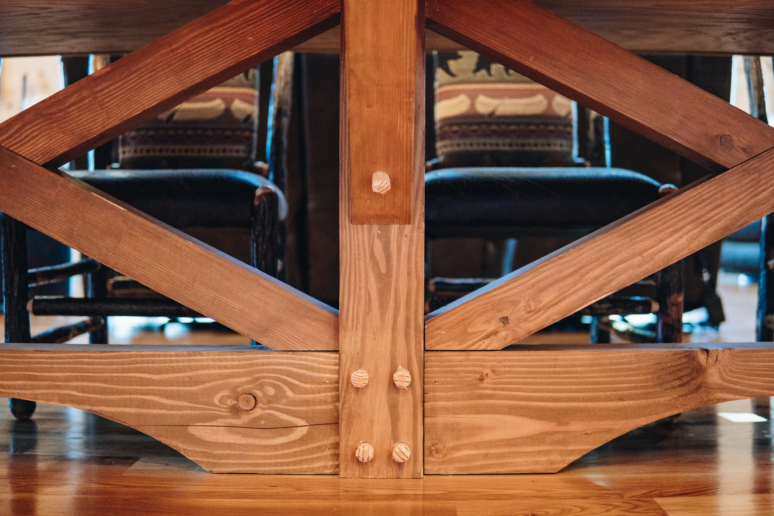 View of a wooden table base with chairs in the background.
