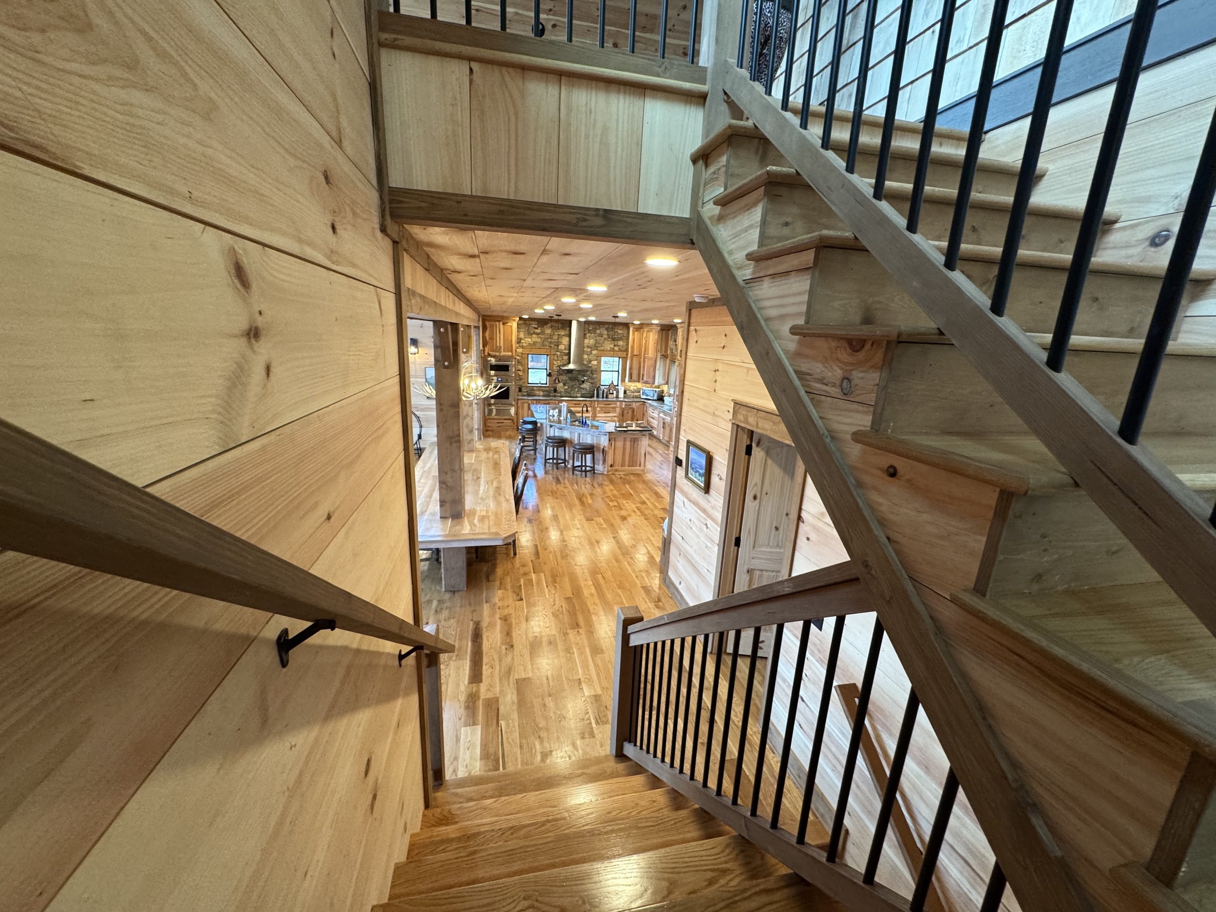 View of a wooden staircase looking down into a spacious, open-concept kitchen and dining area with wooden floors and cabinetry.