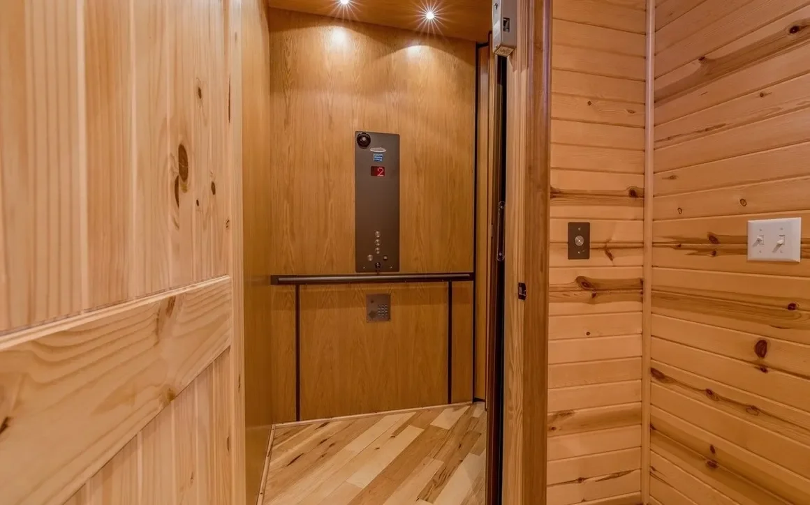 Wood-paneled elevator interior with control panel, handrail, and lighting.