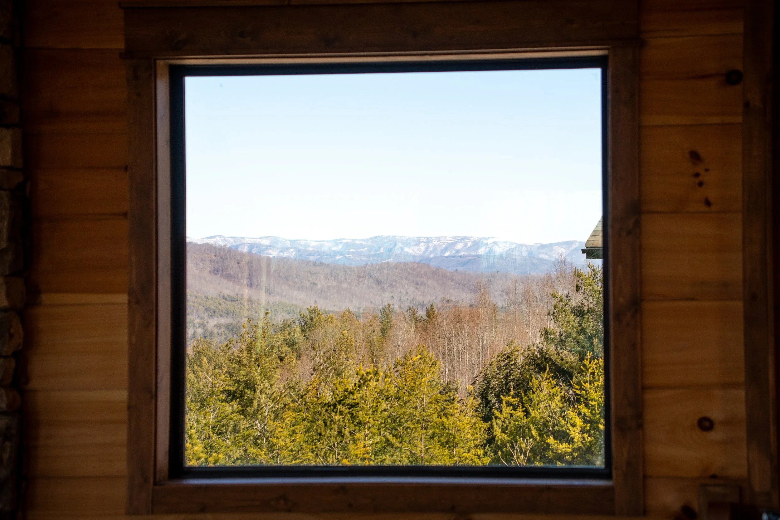 View of distant mountains and forest through a window in a wooden cabin.