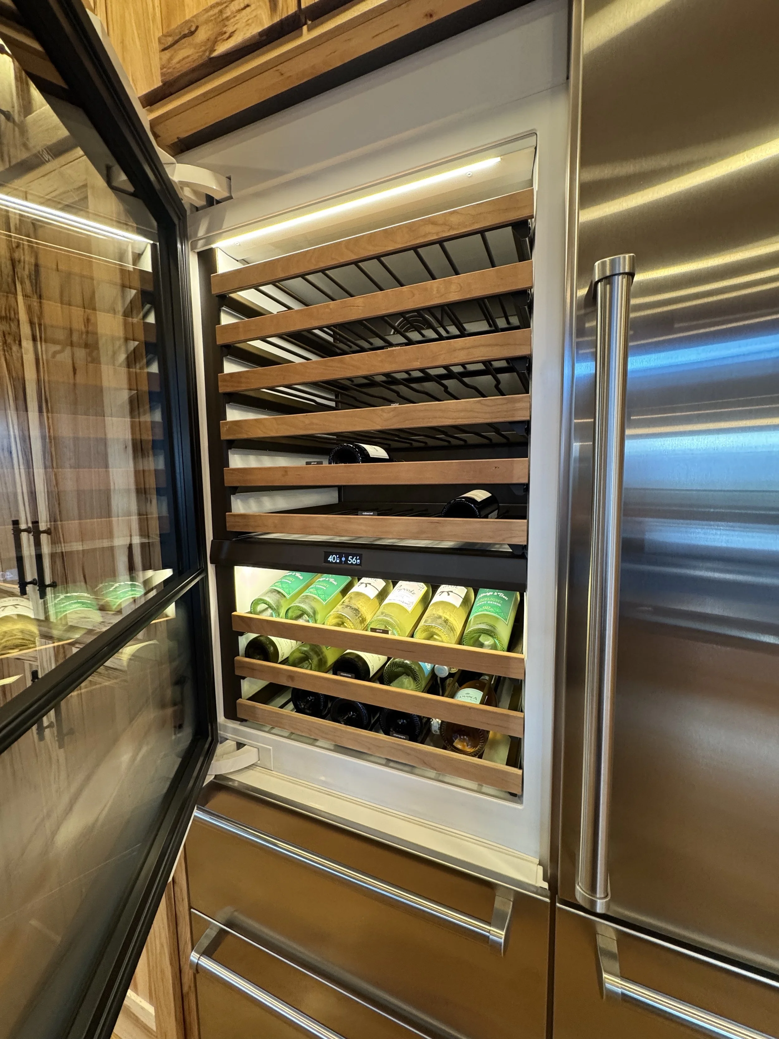 Interior of a wine fridge with several bottles of white wine stored horizontally on wooden racks.