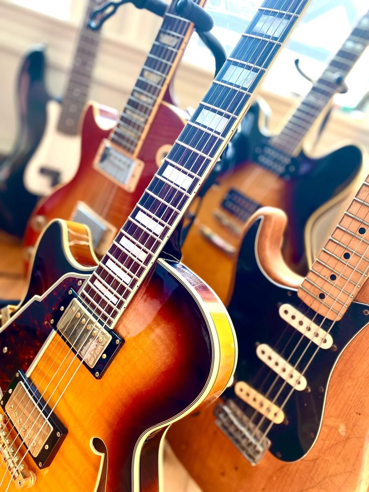A display of multiple electric and acoustic guitars hanging and standing, featuring various body shapes, colors, and fretboard designs.