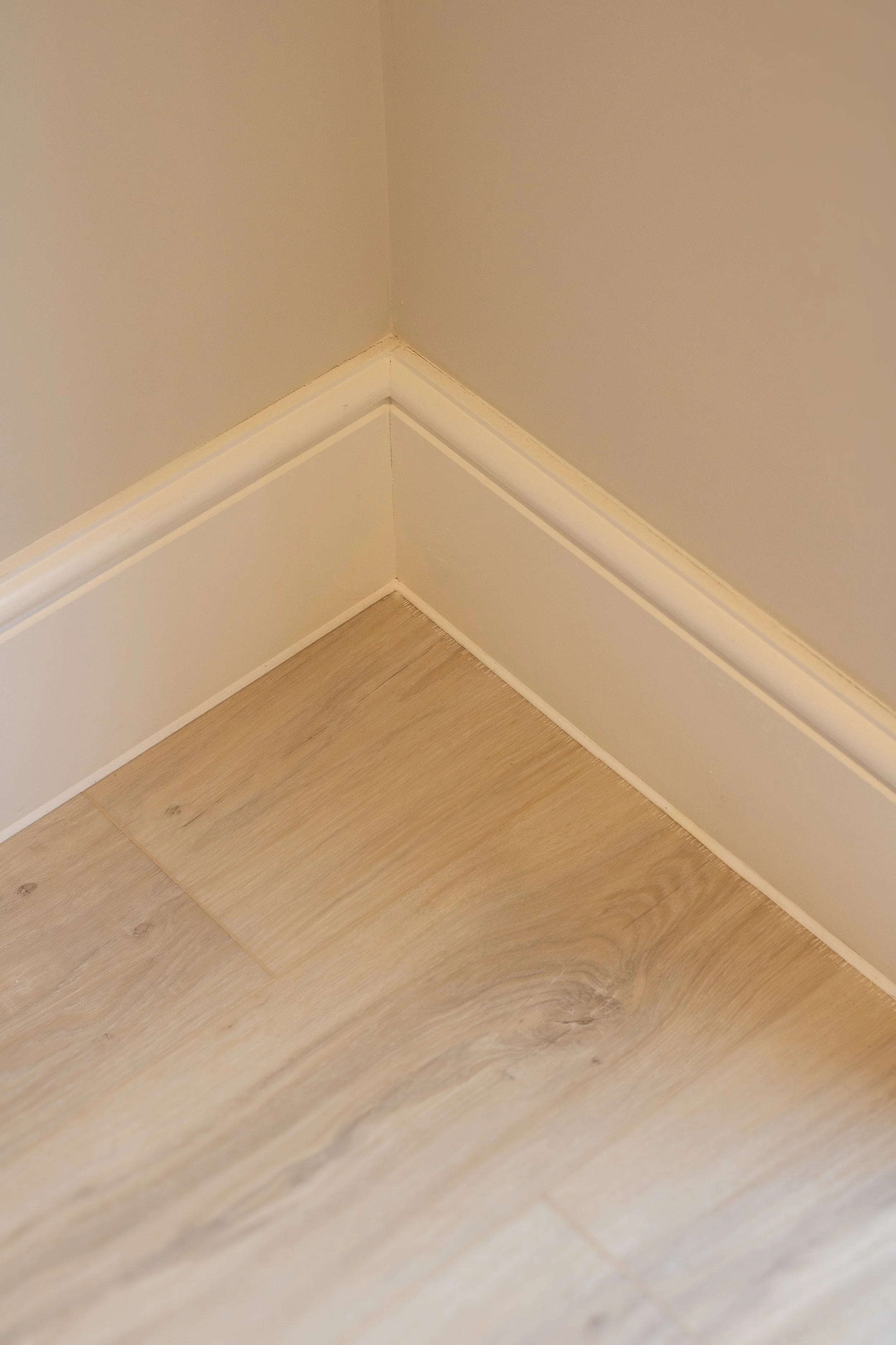 Close-up of a corner where the wall meets the wooden floor, with white baseboard molding.
