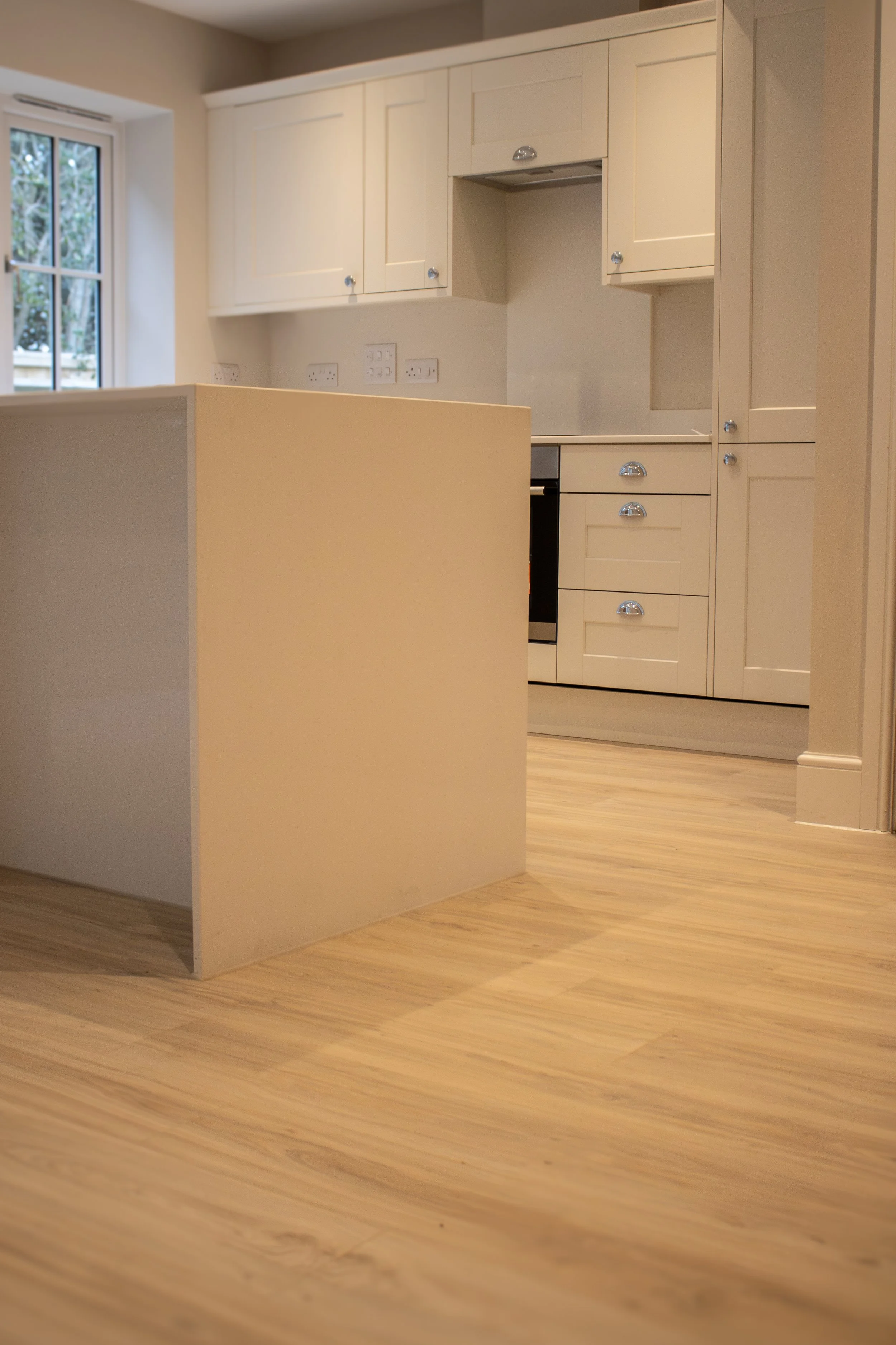 Empty kitchen with white cabinets, wooden flooring, and a small island or counter in the foreground.