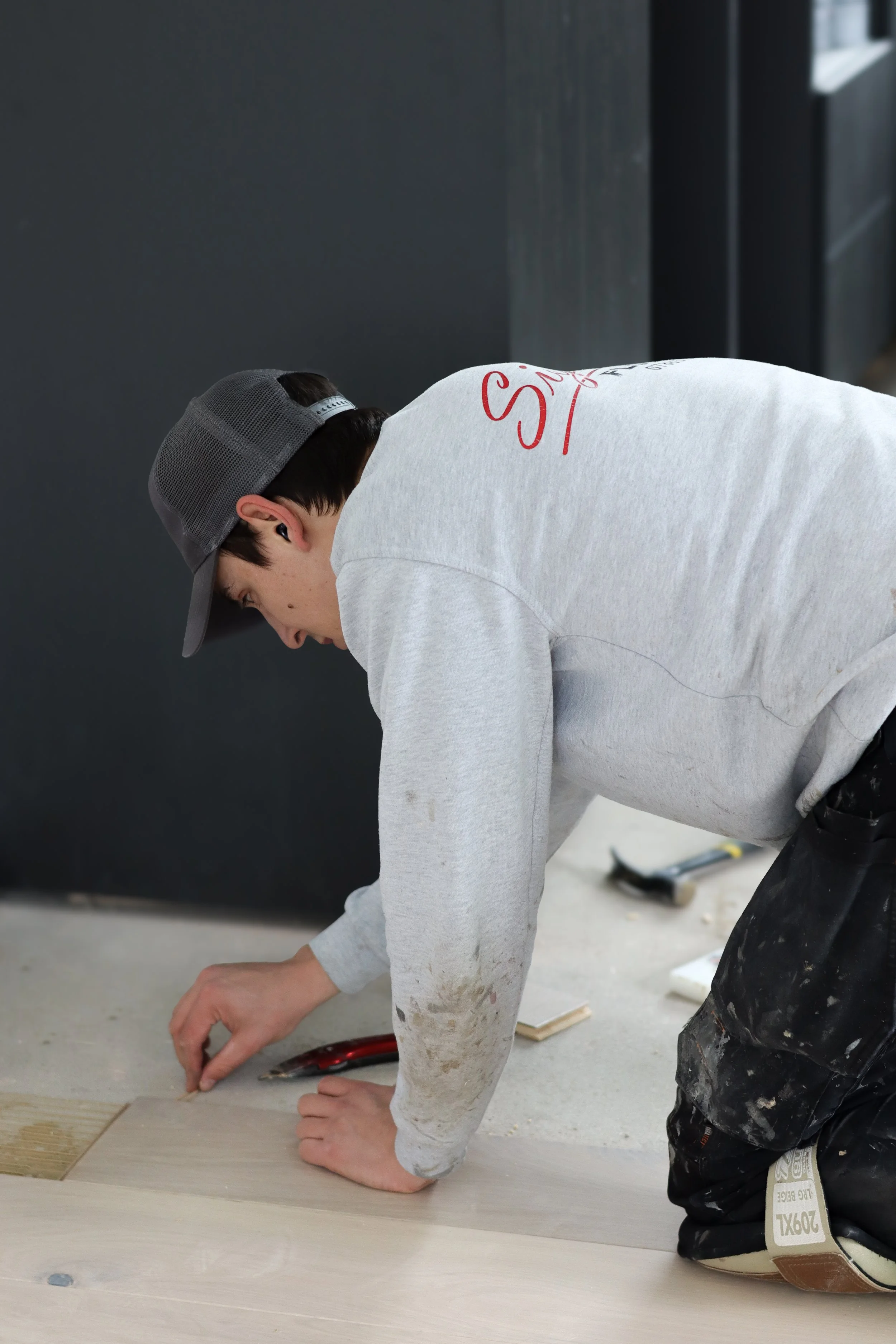 Modern kitchen with a white marble kitchen island and beige velvet chairs with gold bases, a large vase with dried leaves, and a light wood herringbone floor.
