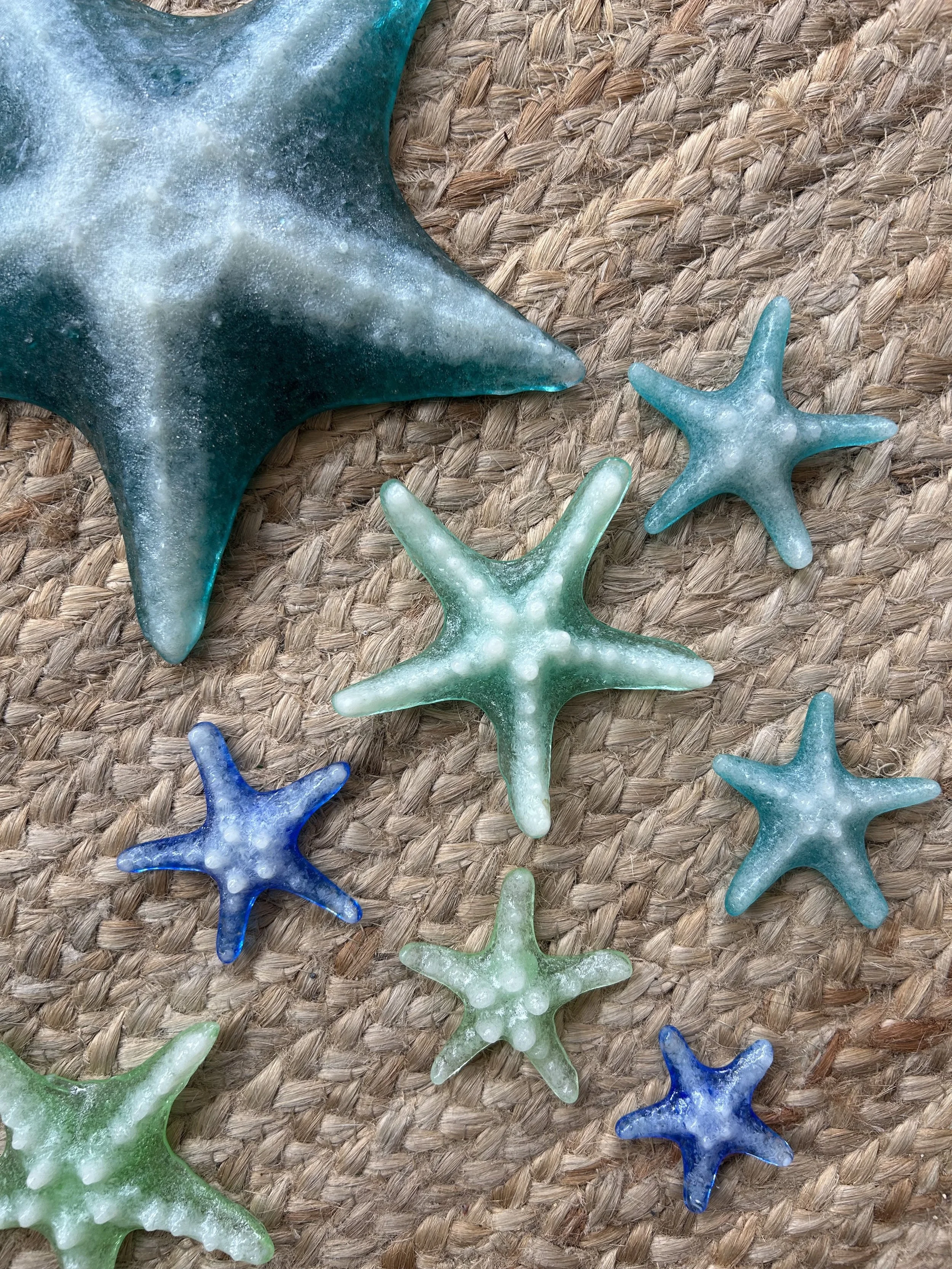 Various colorful starfish decorations, including large green and blue starfish, on a woven straw surface.
