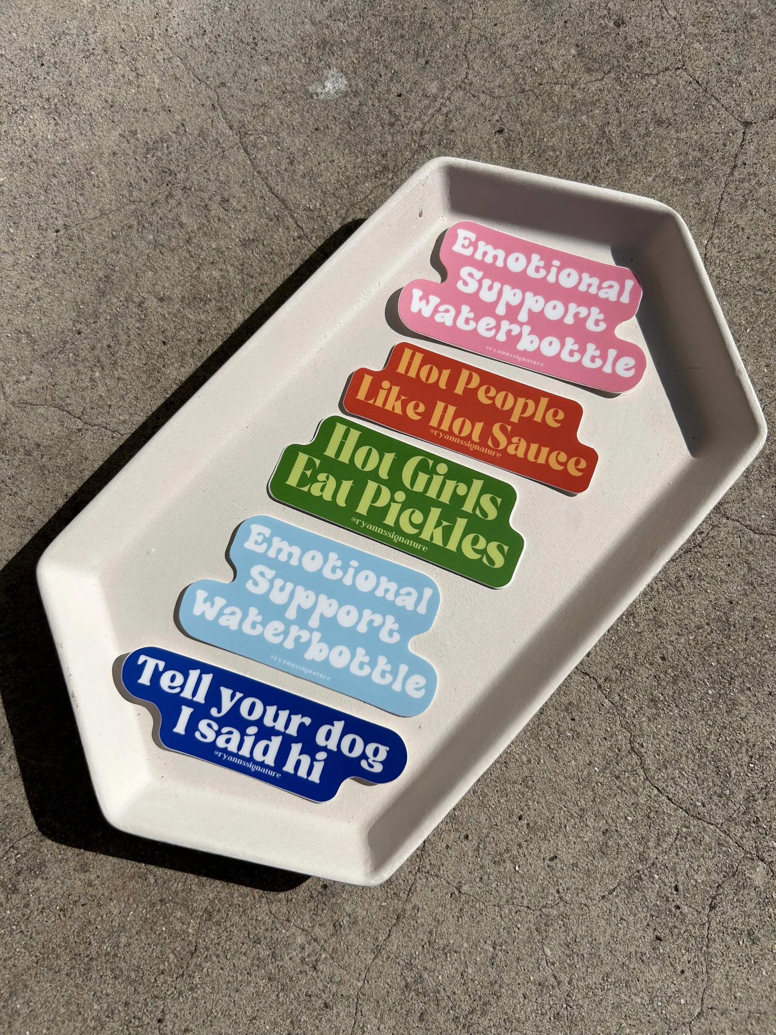 A white tray with colorful stickers that have humorous phrases, including: 'Emotional Support Waterbottle,' 'Hot People Like Hot Sauce,' 'Hot Girls Eat Pickles,' and 'Tell your dog I said hi.'