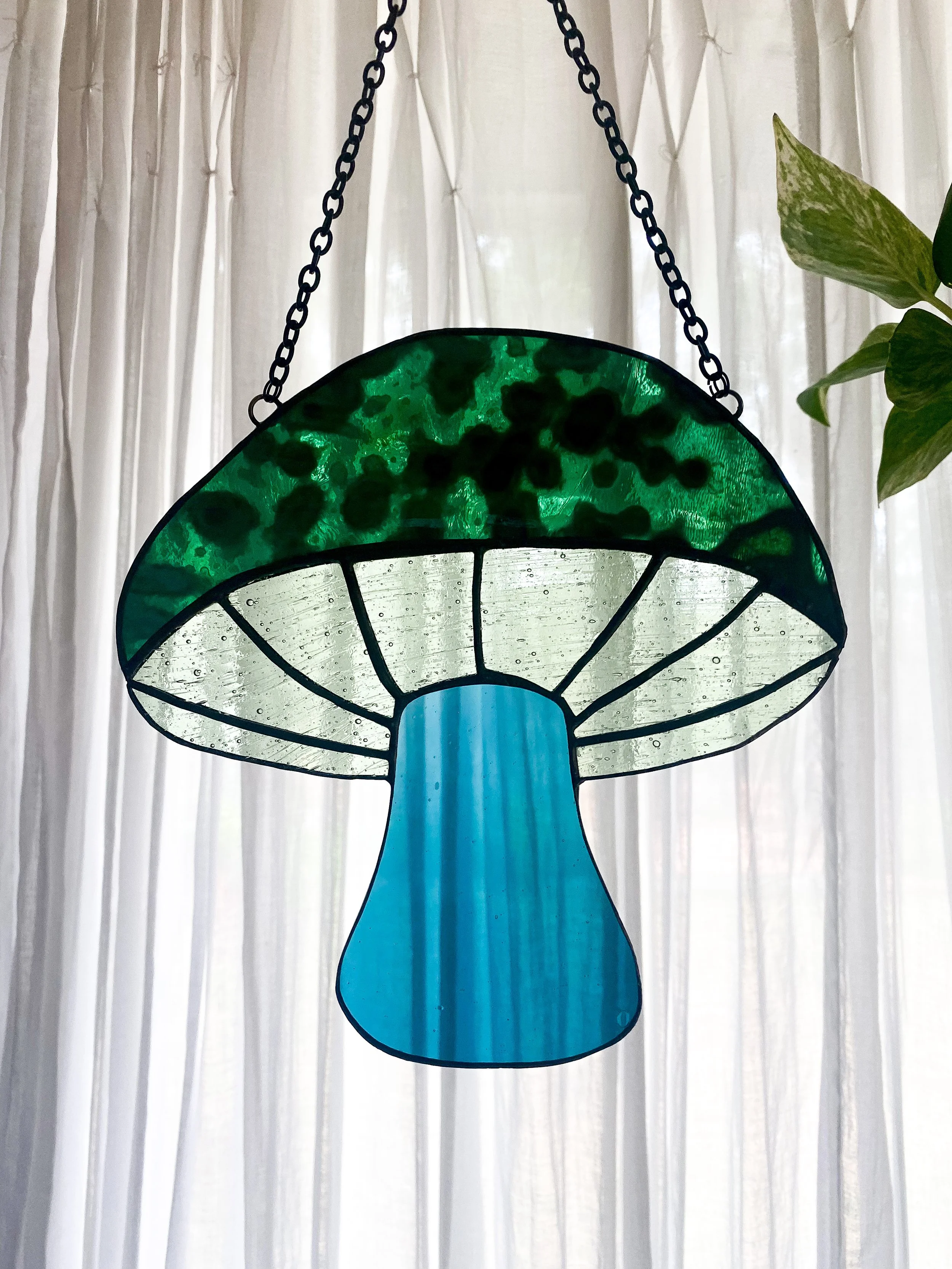 Colorful stained glass lamp in the shape of a mushroom hanging in front of sheer curtains