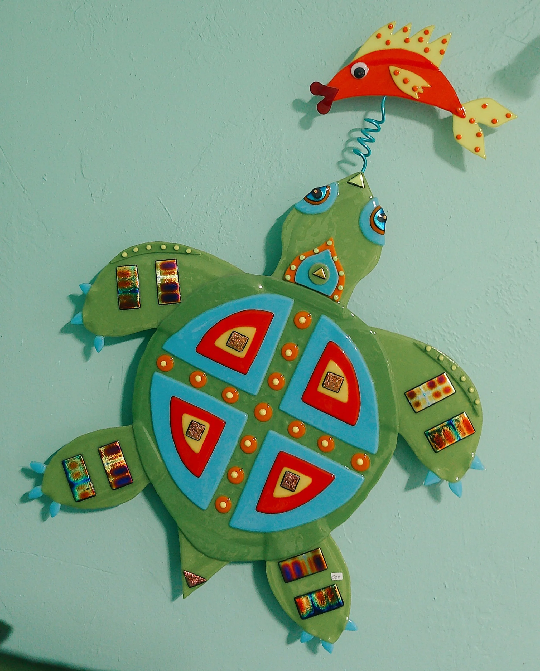 Colorful metal wall art of a turtle with a fish attached by a spring.