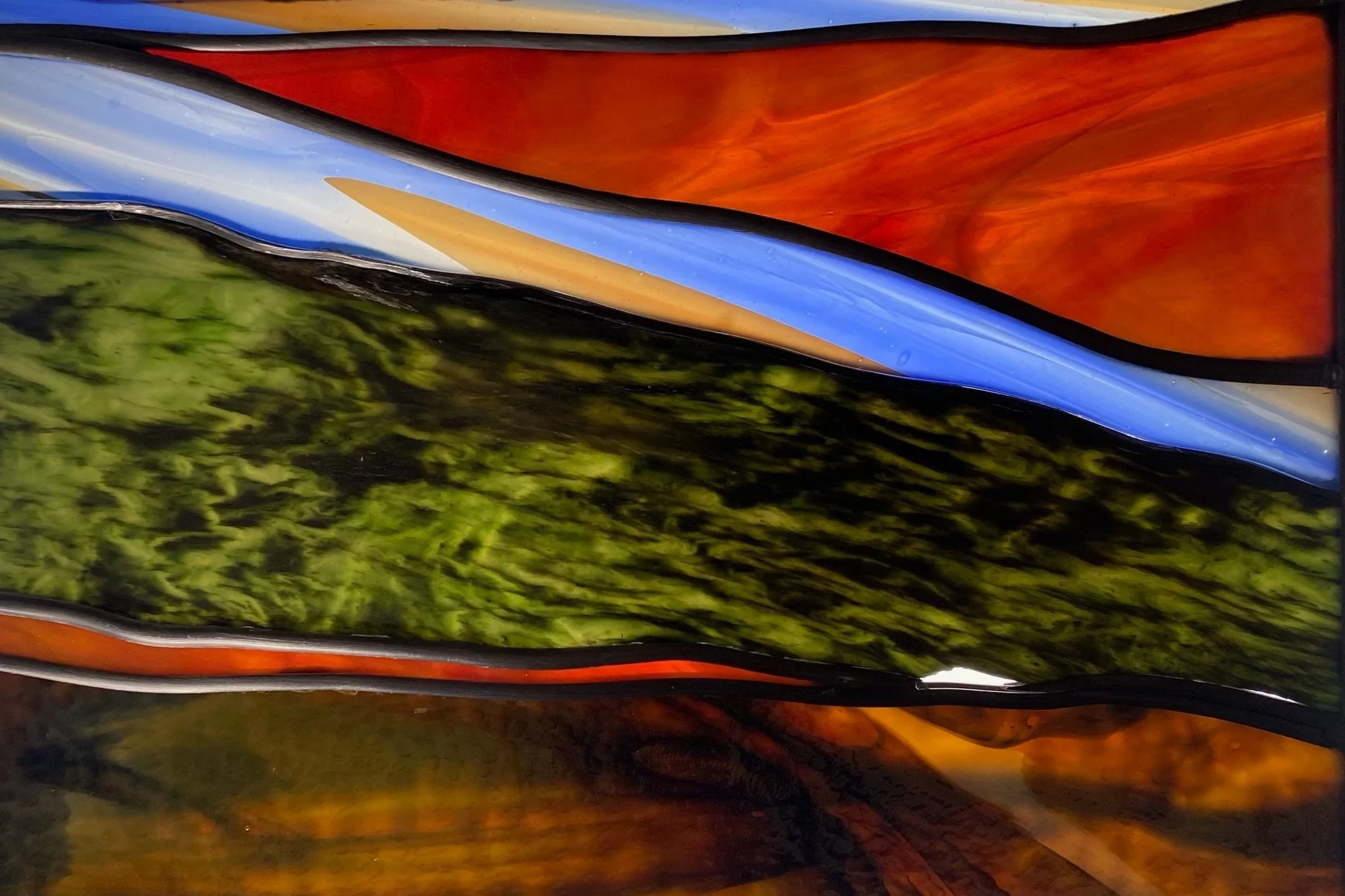 Close-up of a colorful, abstract stained glass window with various shades of orange, blue, green, and black.