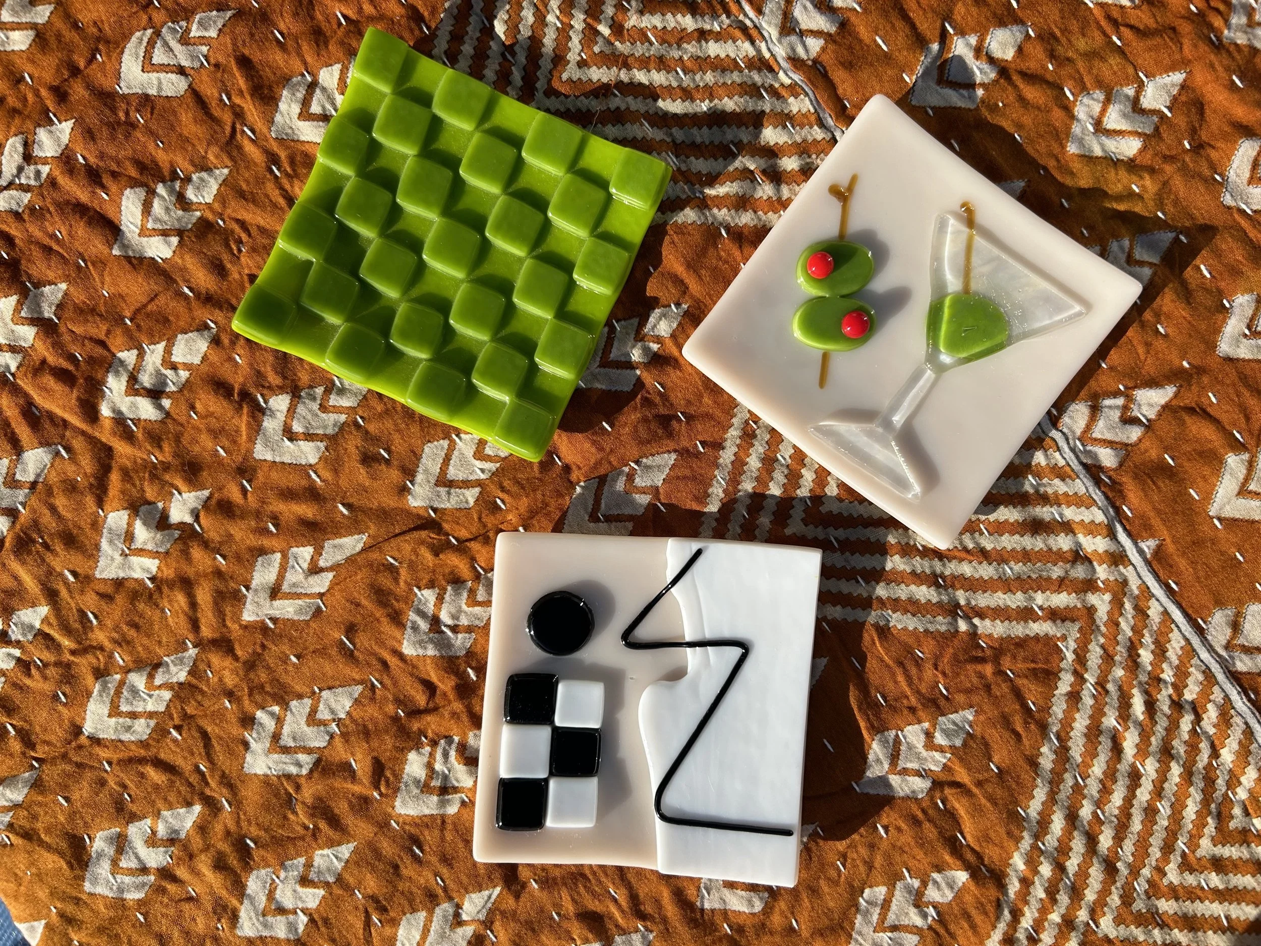 Colorful abstract ceramic tiles with geometric shapes on a patterned fabric background.