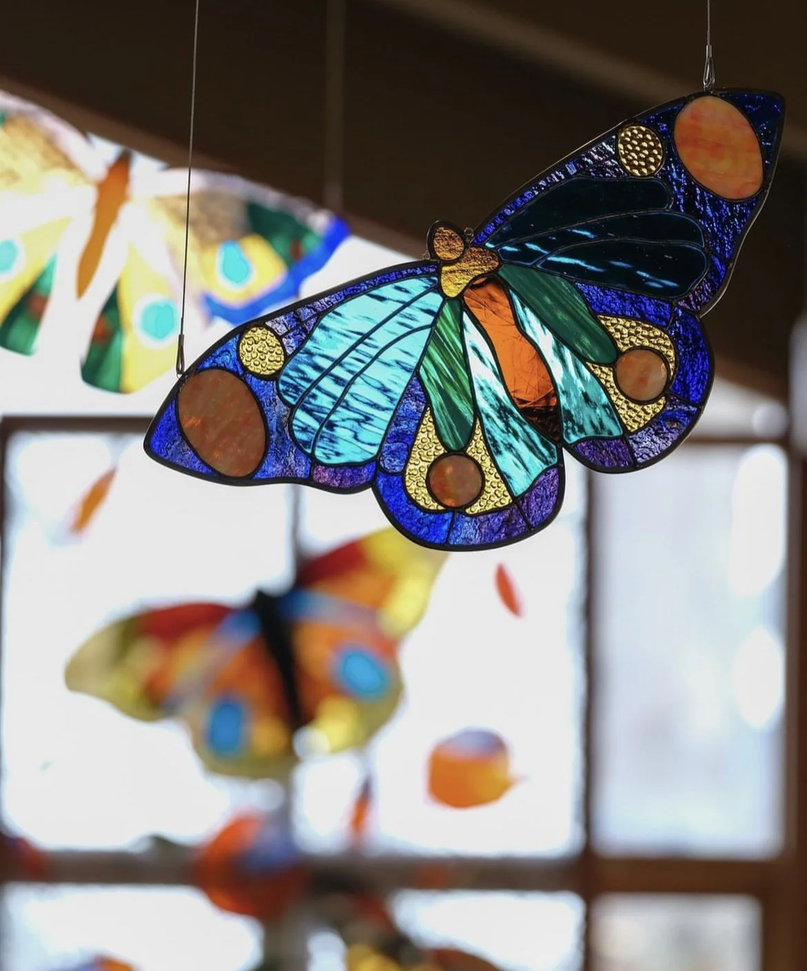 Colorful stained glass butterfly hanging ornament with other butterfly decorations in the background.