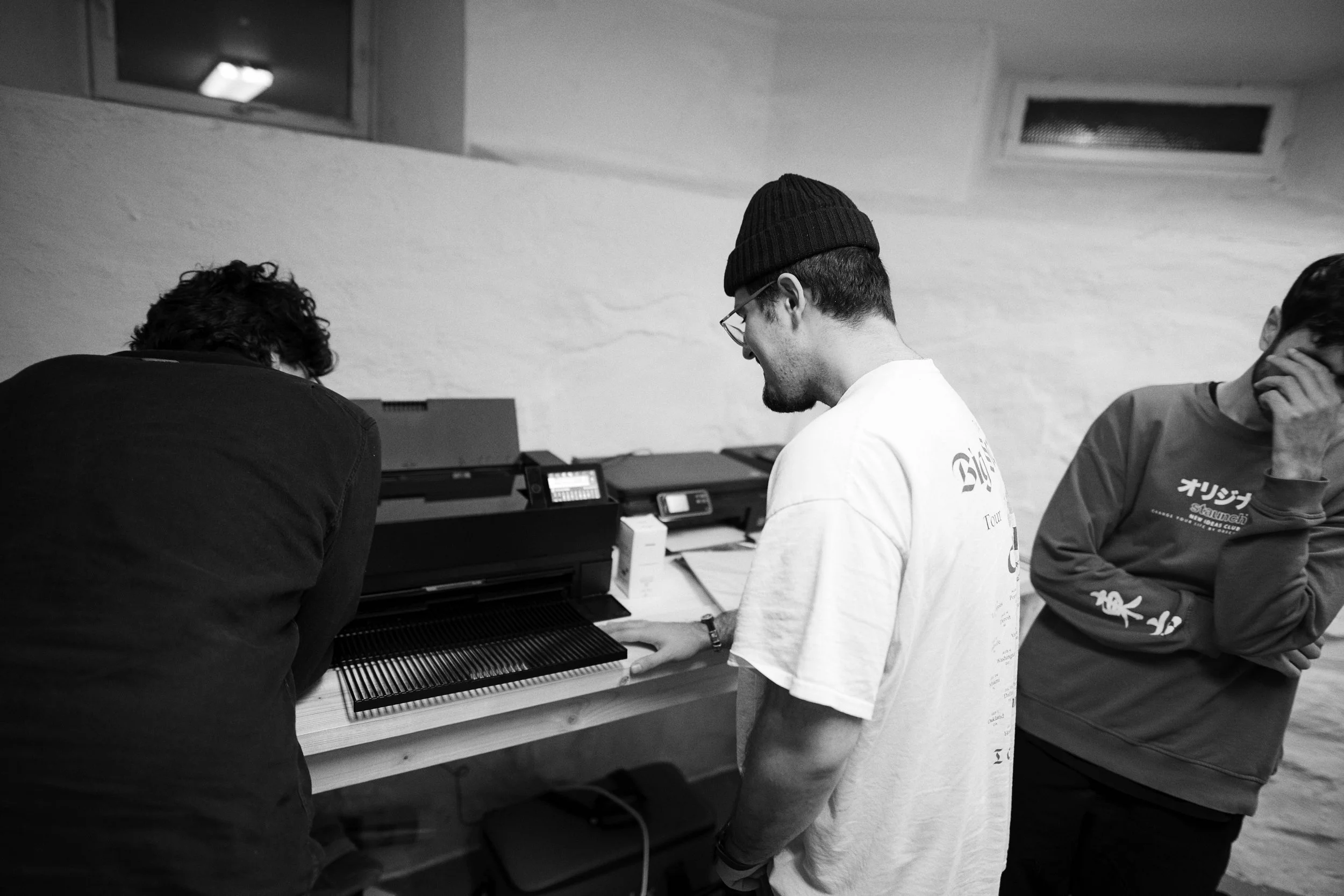 Tre personer ser på en printer i et verksted.