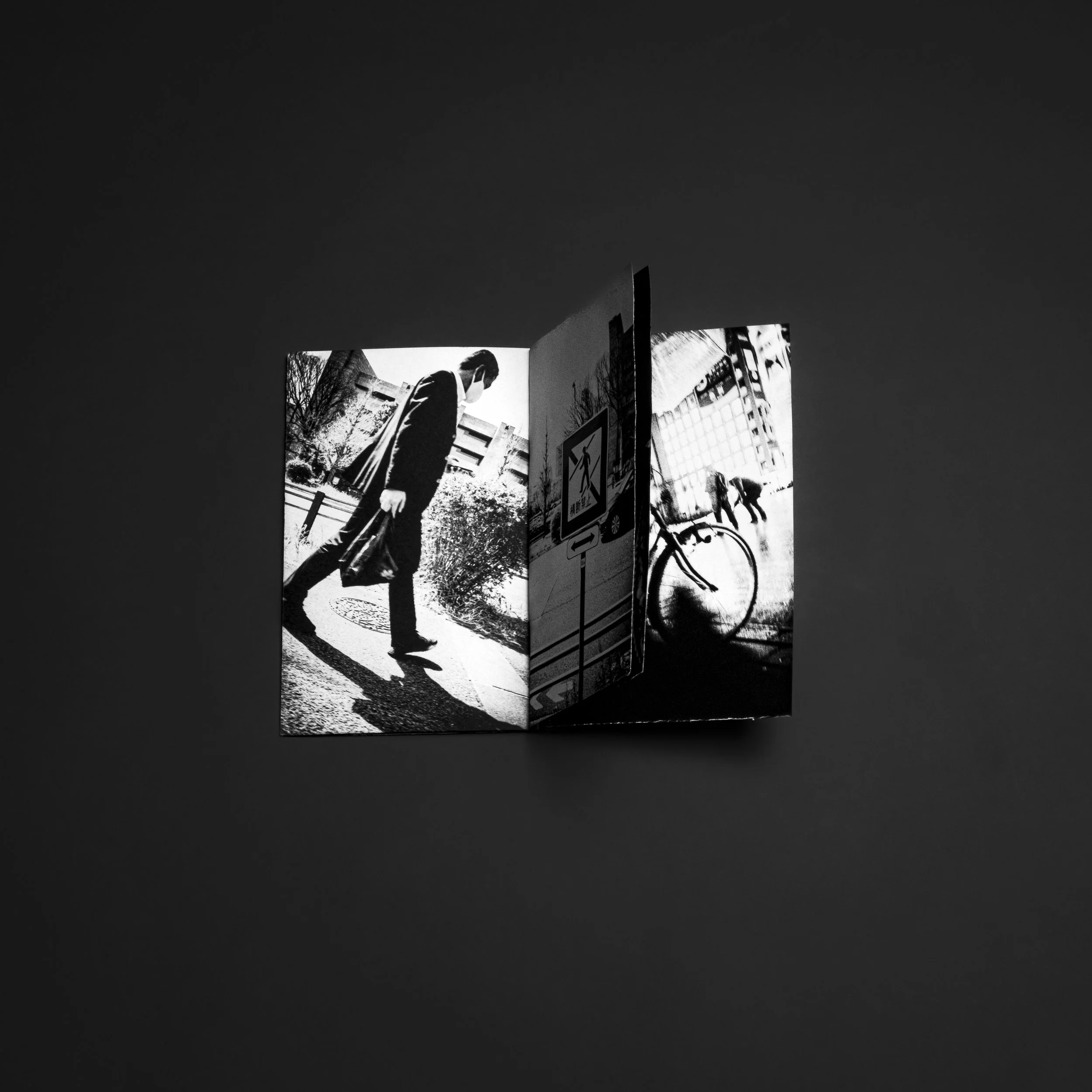 Black and white photograph of an open booklet with images of a man walking and a bicycle, placed on a dark surface.