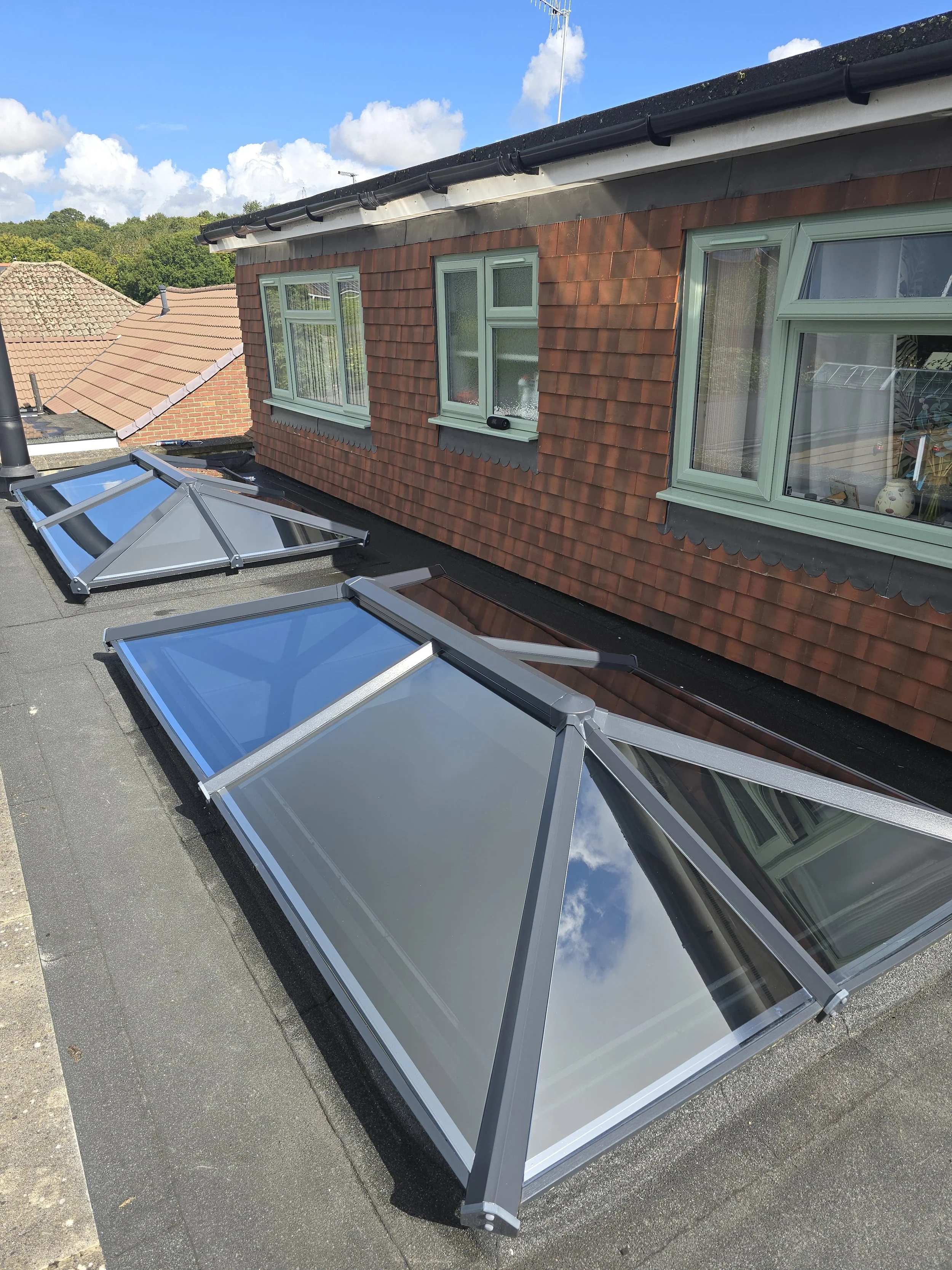 Three skylights on a flat rooftop of a building with a brick exterior and green window frames.