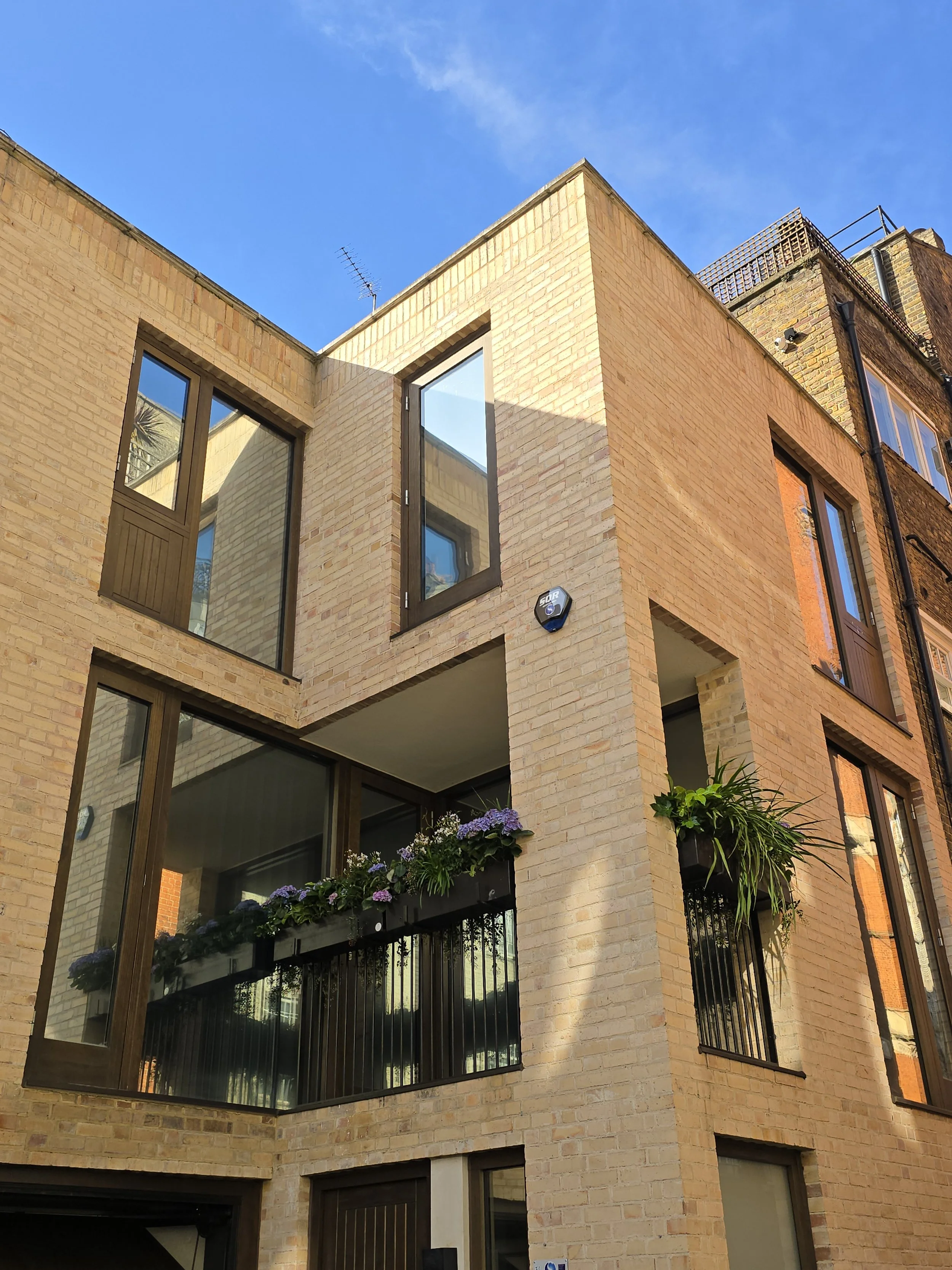 Bright yellow brick apartment building with large windows, flower boxes, and plant decorations on a sunny day.