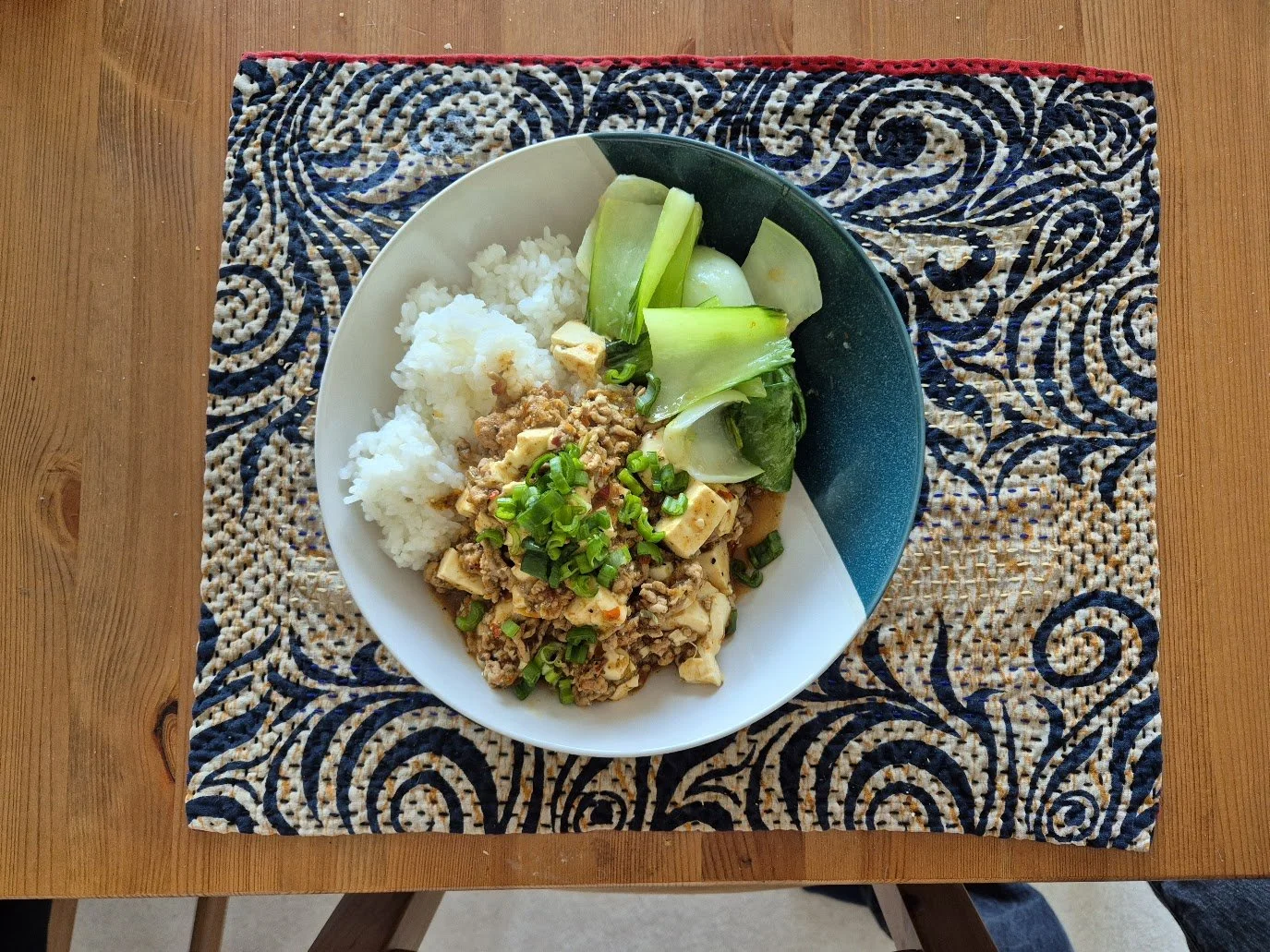 A bowl of white rice, tofu with ground meat and chopped green onions, and a side of cucumber and bok choy on a decorative placemat.