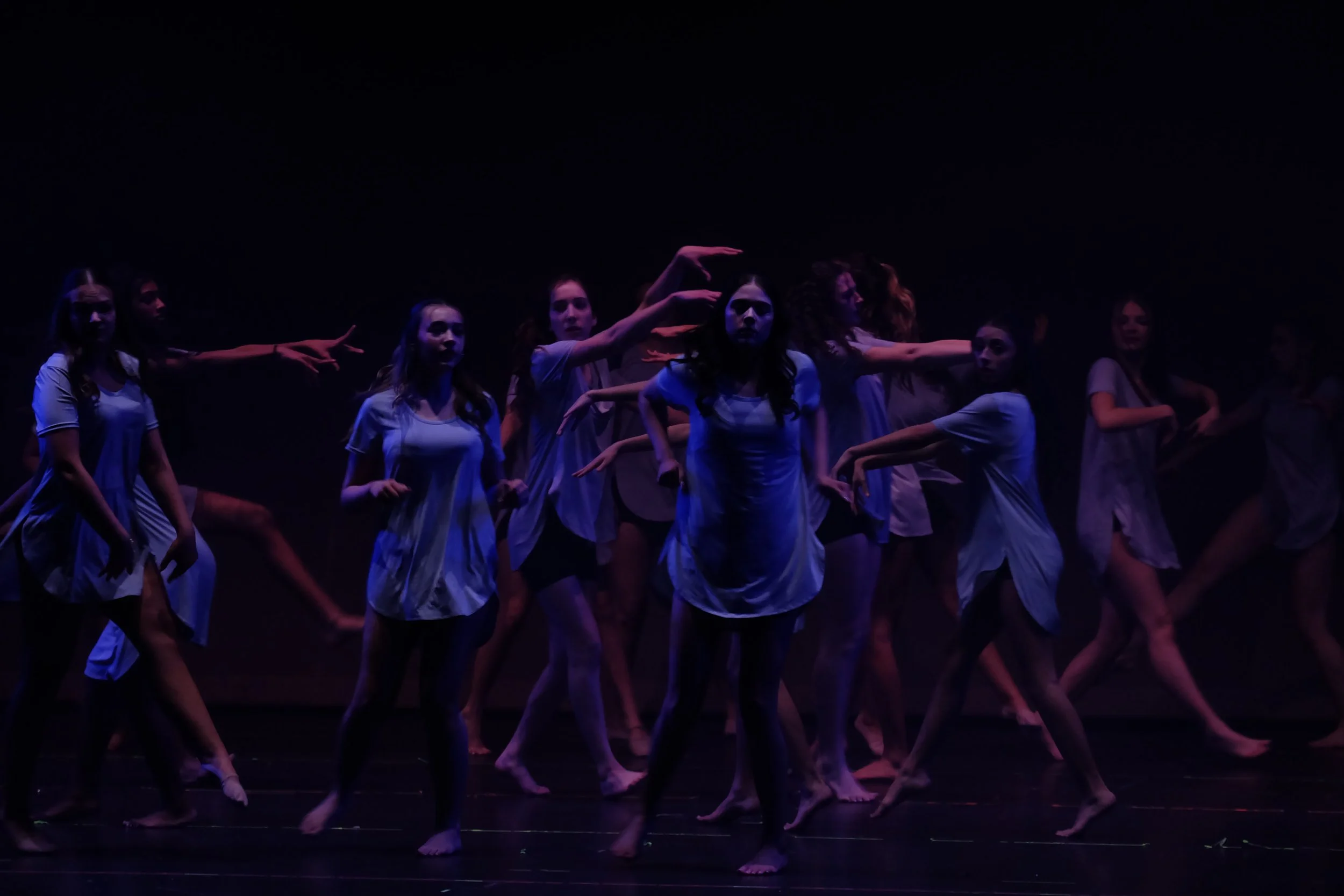 A group of female dancers performing on stage in white costumes under dim lighting.