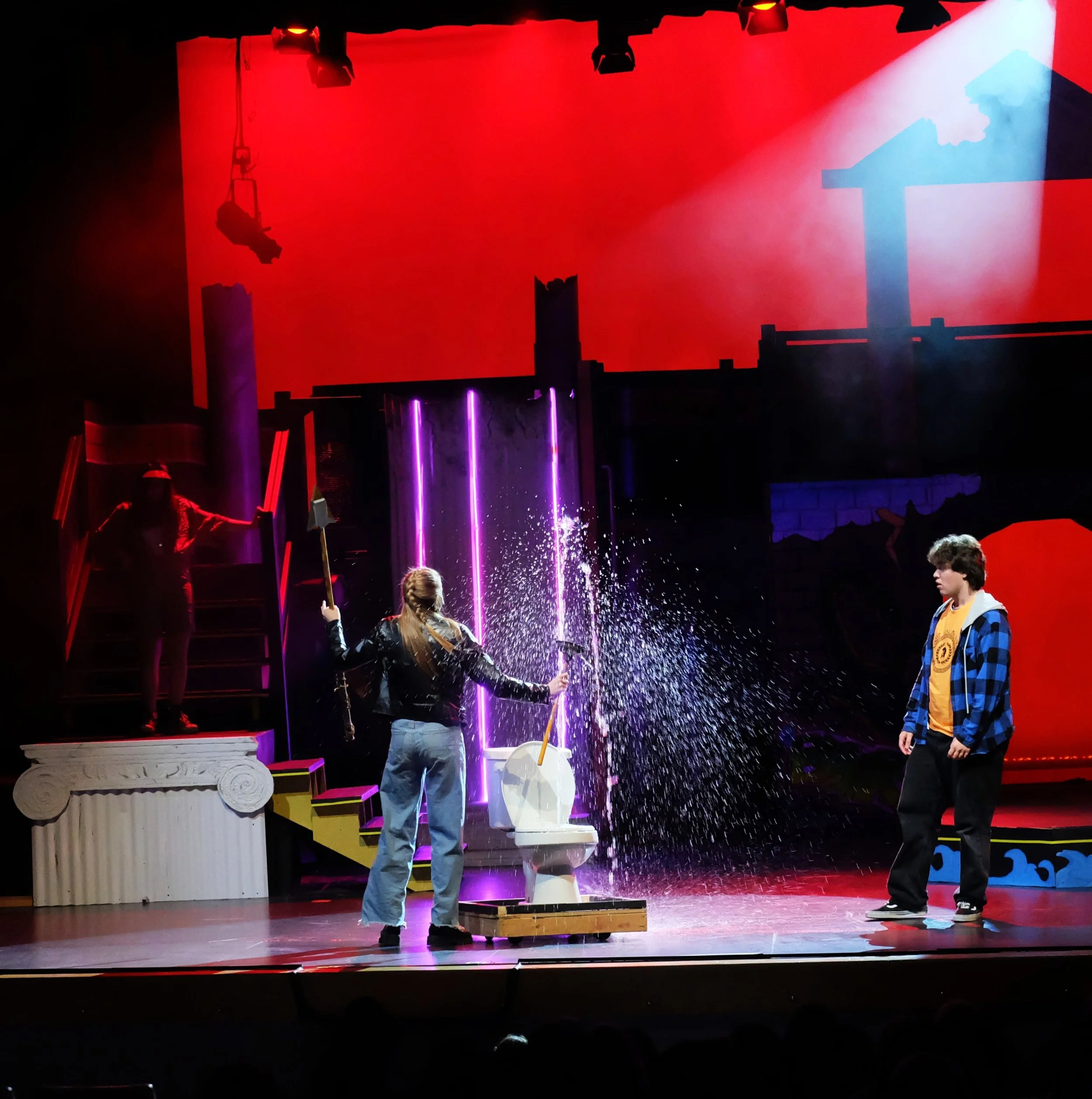 Stage scene with performers and props, bright lights, and a red background as part of a show or performance.