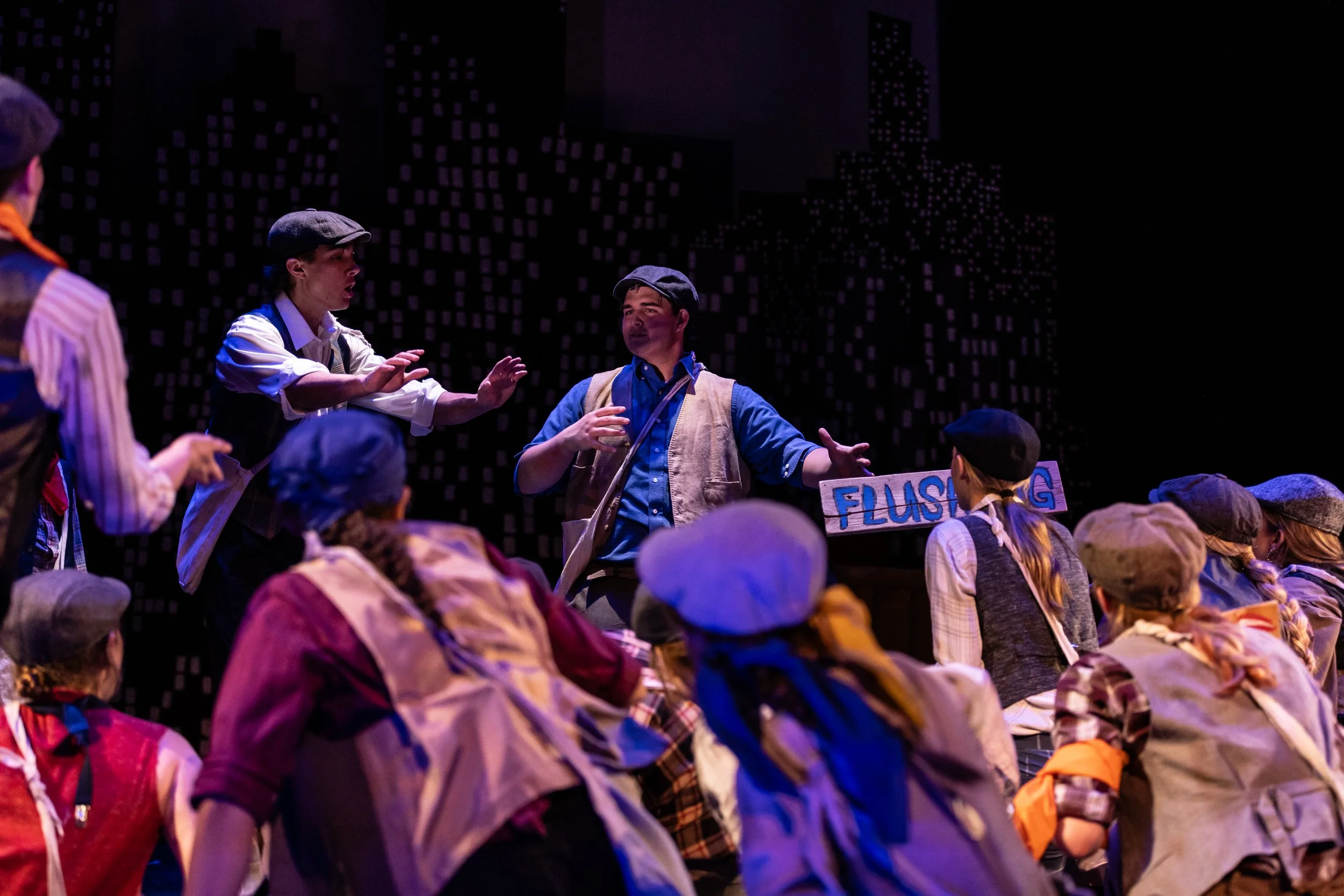 Performers dressed as pioneers speaking to a group of children during a stage performance.