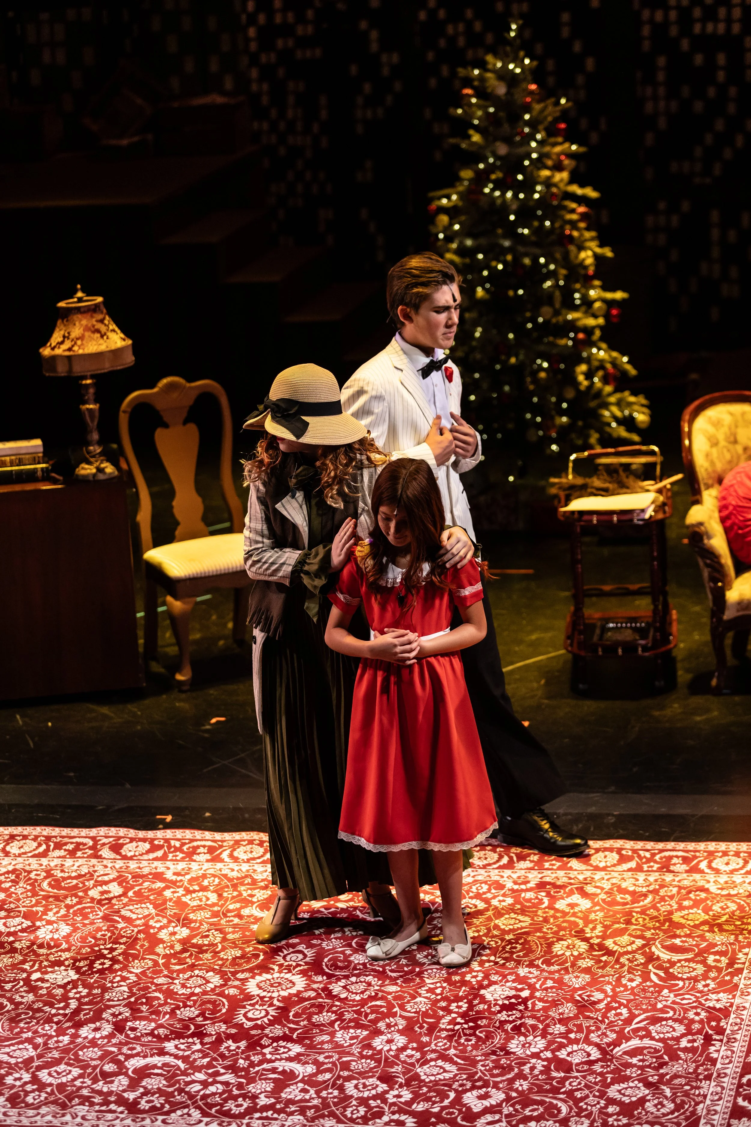 People dressed in vintage clothing performing on stage with a Christmas tree in the background.