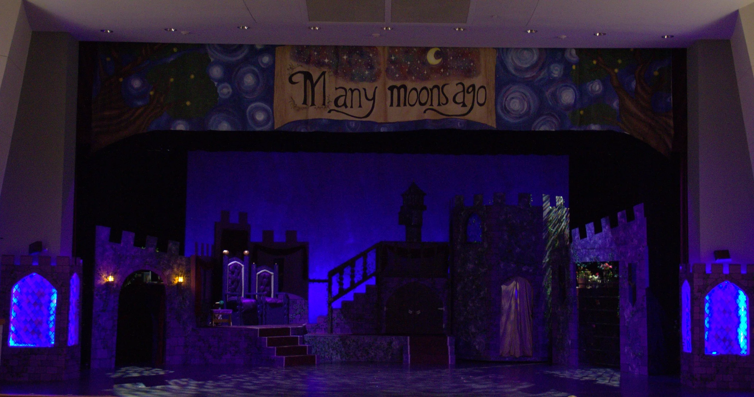 Stage set designed to resemble a castle with purple and blue lighting, featuring a banner that reads 'Many Moons Ago' and artwork of a starry night sky with a crescent moon.