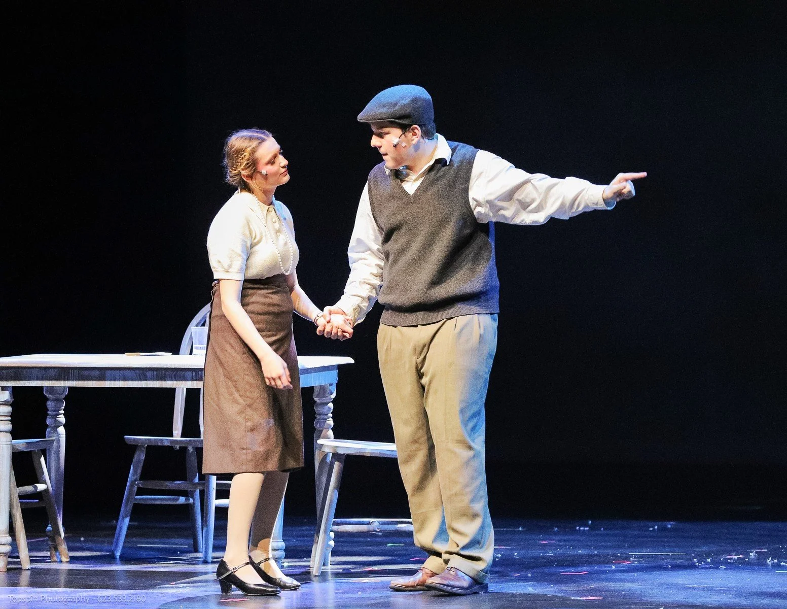 A man and a woman holding hands on stage, with the man pointing forward, likely during a theatrical performance.