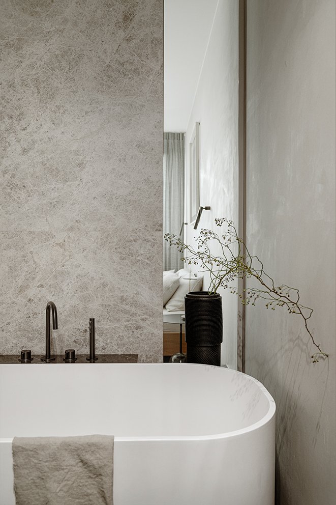 A wooden vase made in wood carving technique by Maciej Gąsienica-Giewont holding a minimal ikebana arrangement. Placed on a shelf in a bathroom with a freestanding bathtub. Taps by Piet Boon for COCOON Collection. Interior design by Ines Lulkowska.