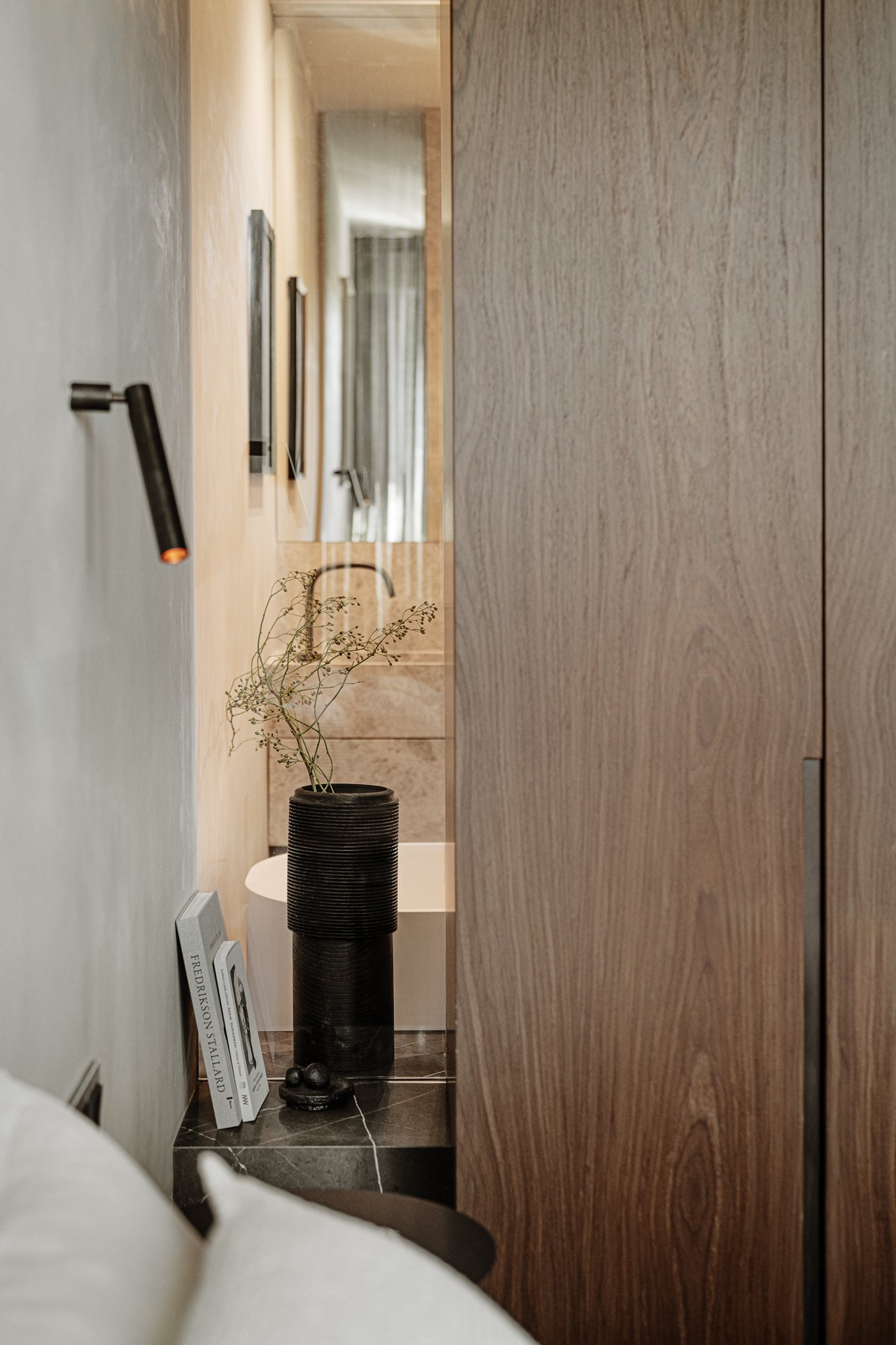 A bathroom with a glass partition to the bedroom, featuring a marble shelf holding a wooden vase by Maciej Gąsienica-Giewont.