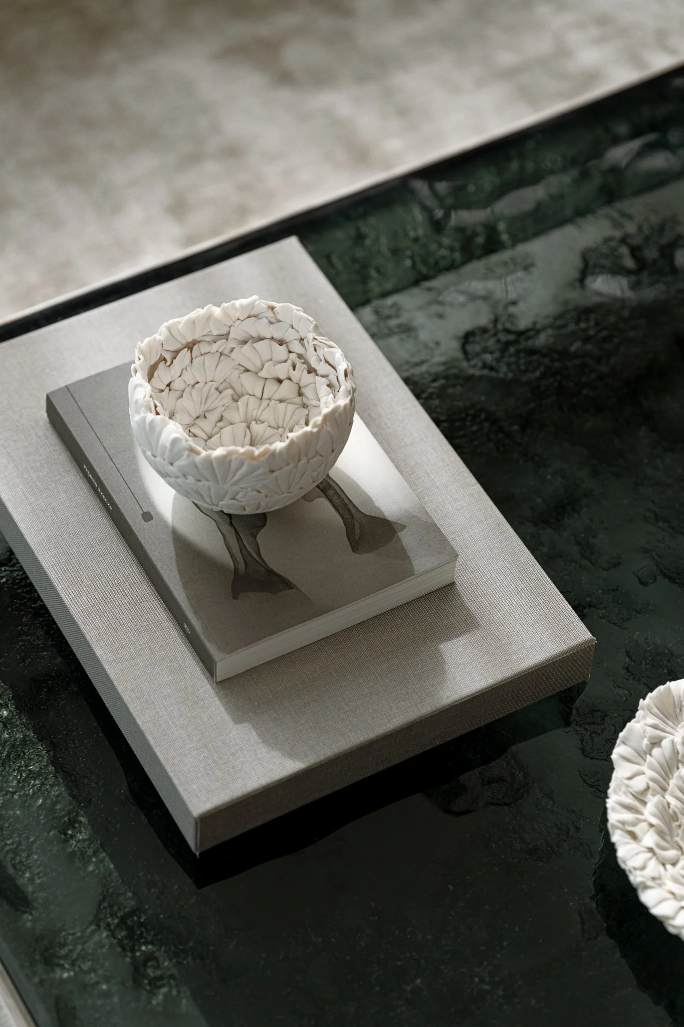 A coffee table by Ines Lulkowska, made of casting anthracite glass framed in stainless steel. Paired with organic-shaped ceramic piece by Elza Jaszczuk, CeramicsMix. The reflections on the table evoke the impression of flowers floating on water.