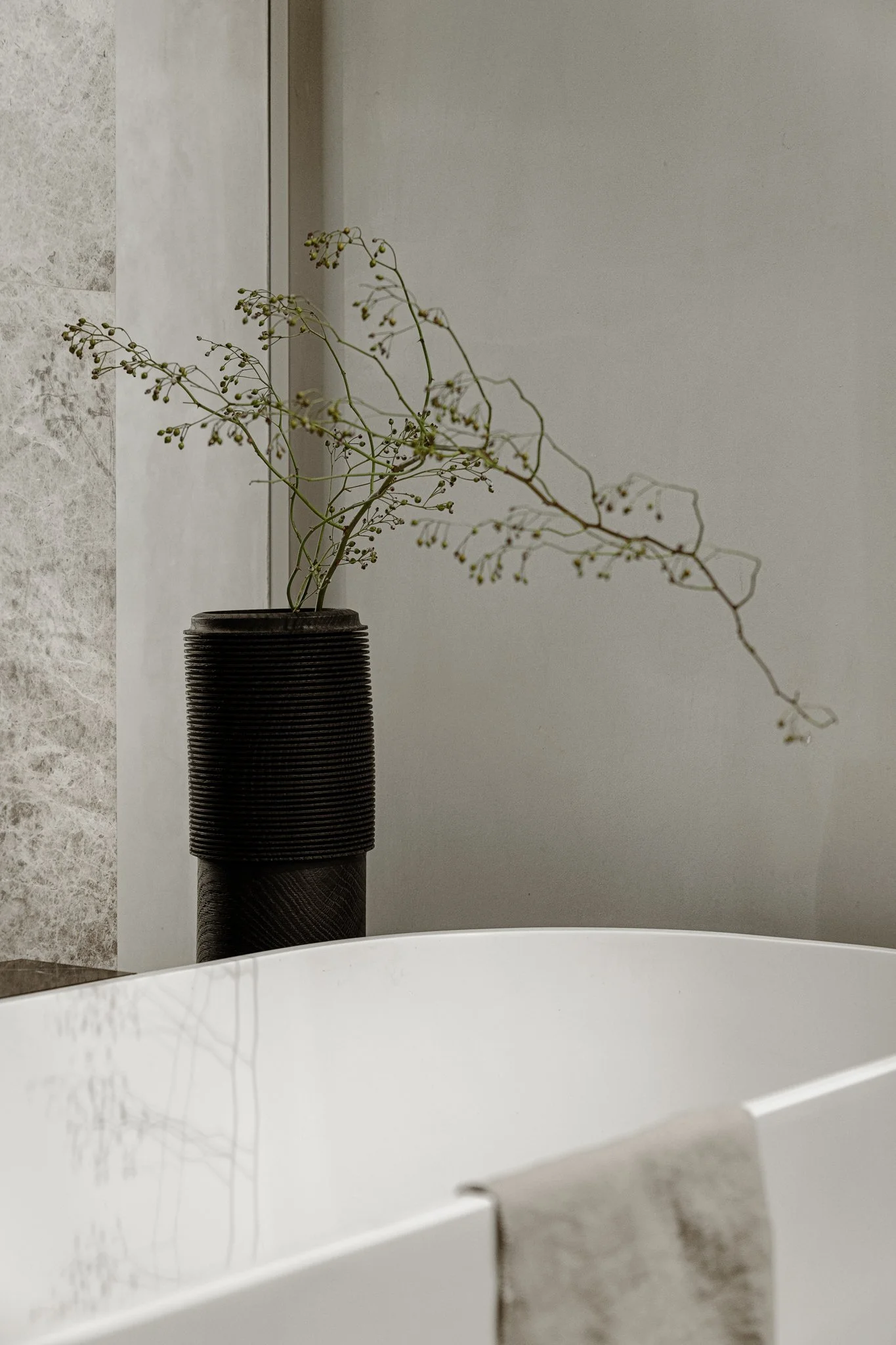 A wooden vase made in wood carving technique by Maciej Gąsienica-Giewont holding a minimal ikebana arrangement. Placed on a shelf in a bathroom with a freestanding bathtub. Interior design by Ines Lulkowska.