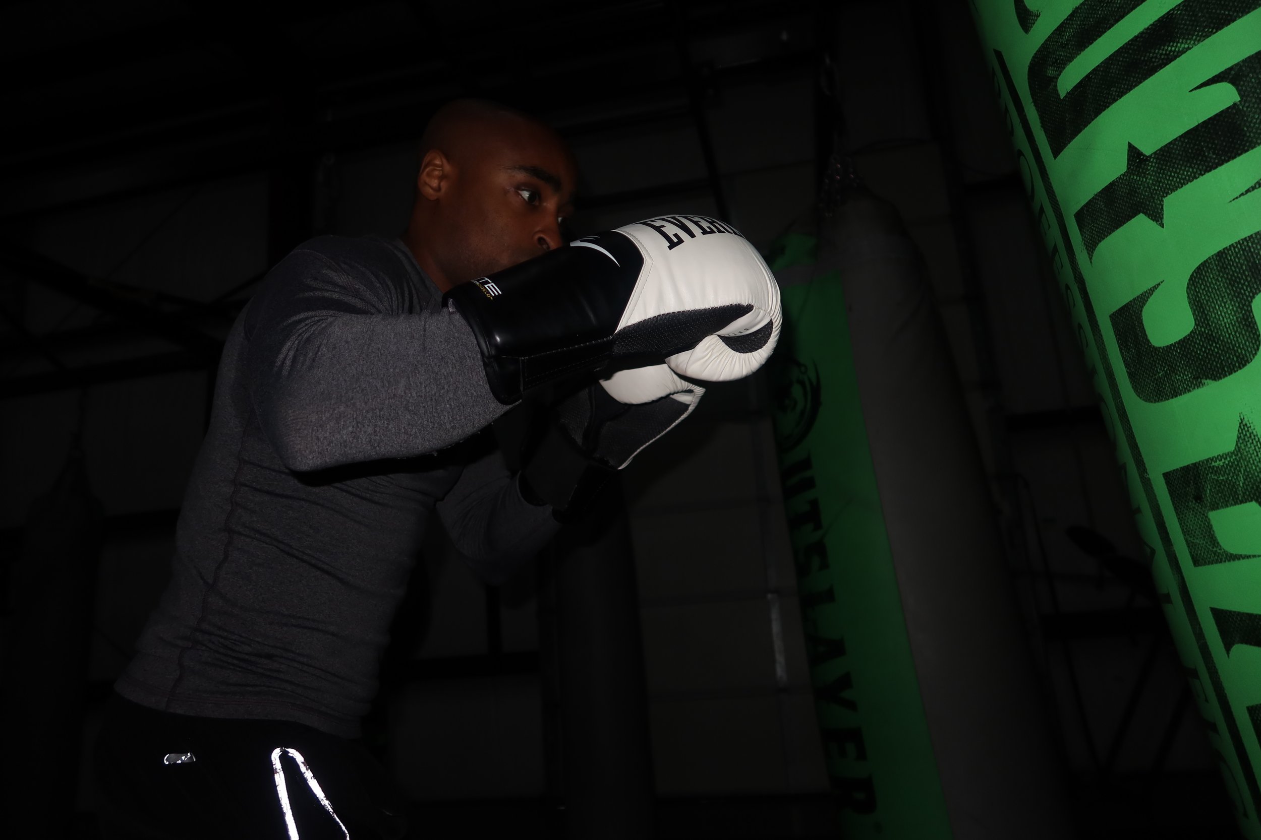 A man in boxing gloves and athletic clothing trains in a boxing gym, throwing a punch at a punching bag.