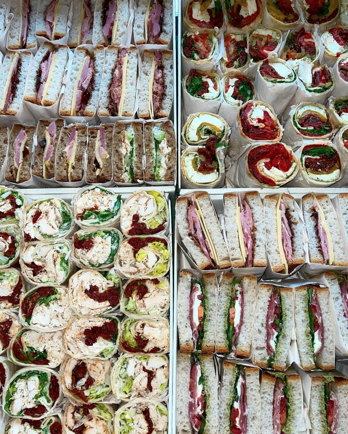 Assorted sandwiches and wrap rolls arranged in trays for display.