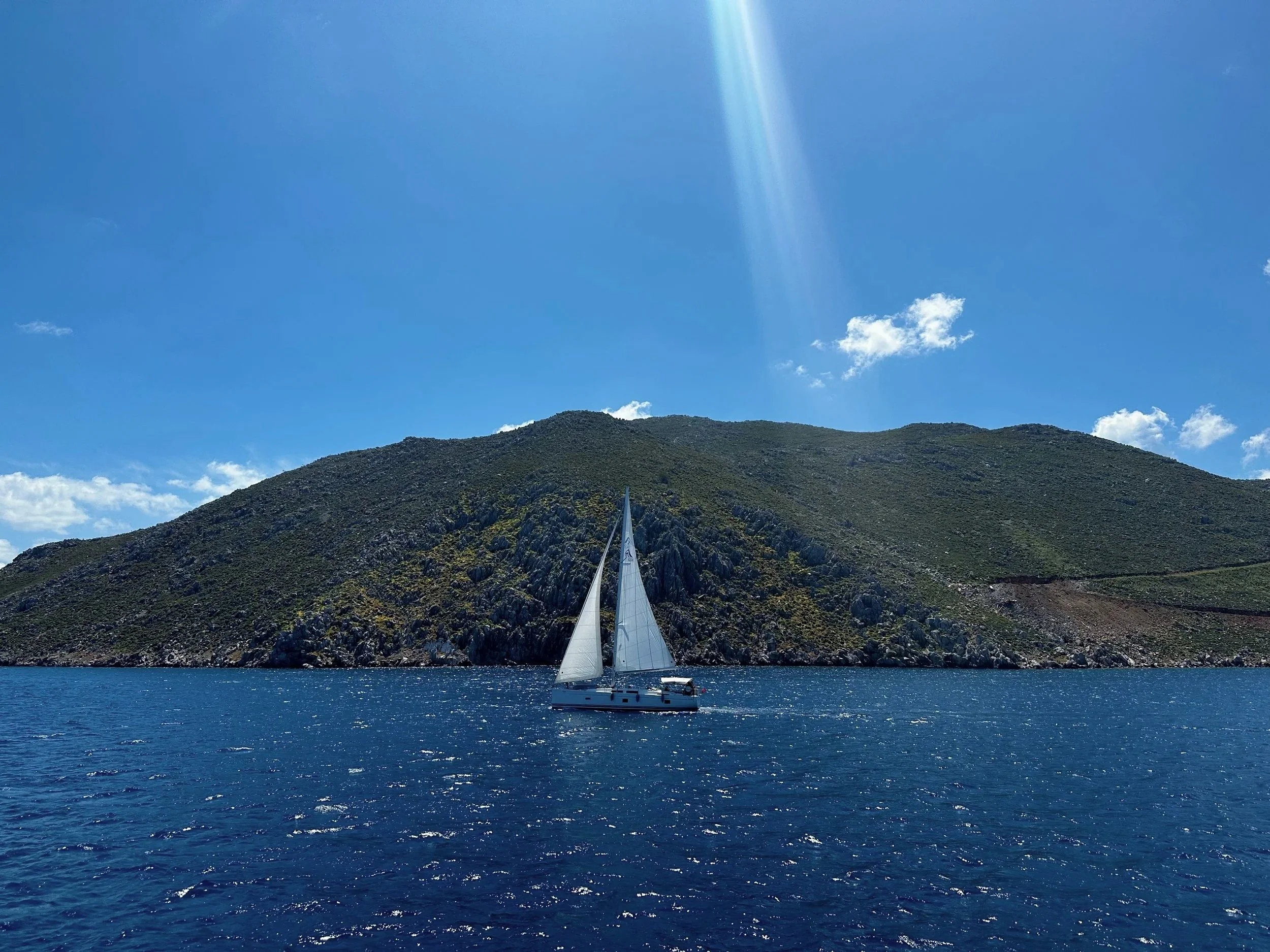 Sailboat drifting along the coast of Symi, Greece on a clear blue day.