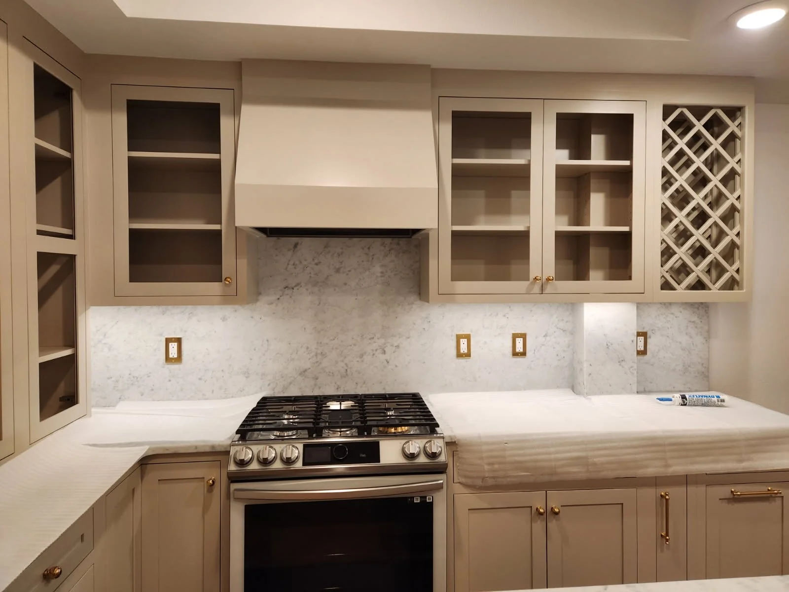 North Idaho Kitchen with beige cabinets, marble backsplash, and a stove installed below open cabinets and wine rack with a tube of sealant on the counter.