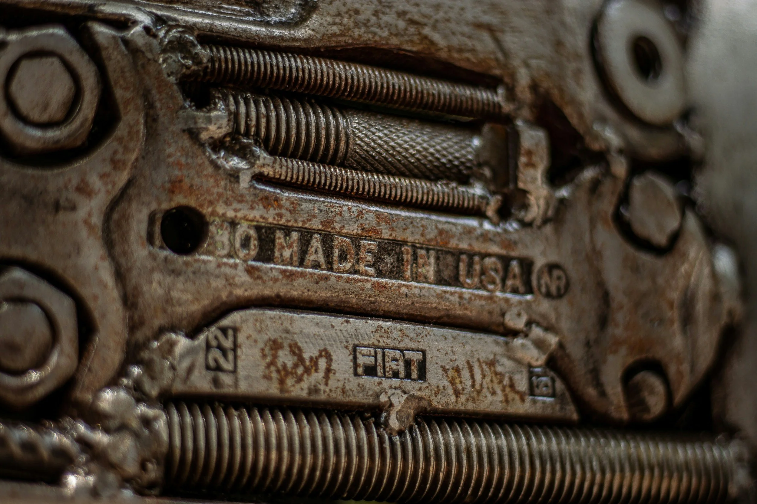 Close-up of a vintage mechanical part with rust, featuring metal springs and stamped markings including 'Made in USA' and 'Fiat'.
