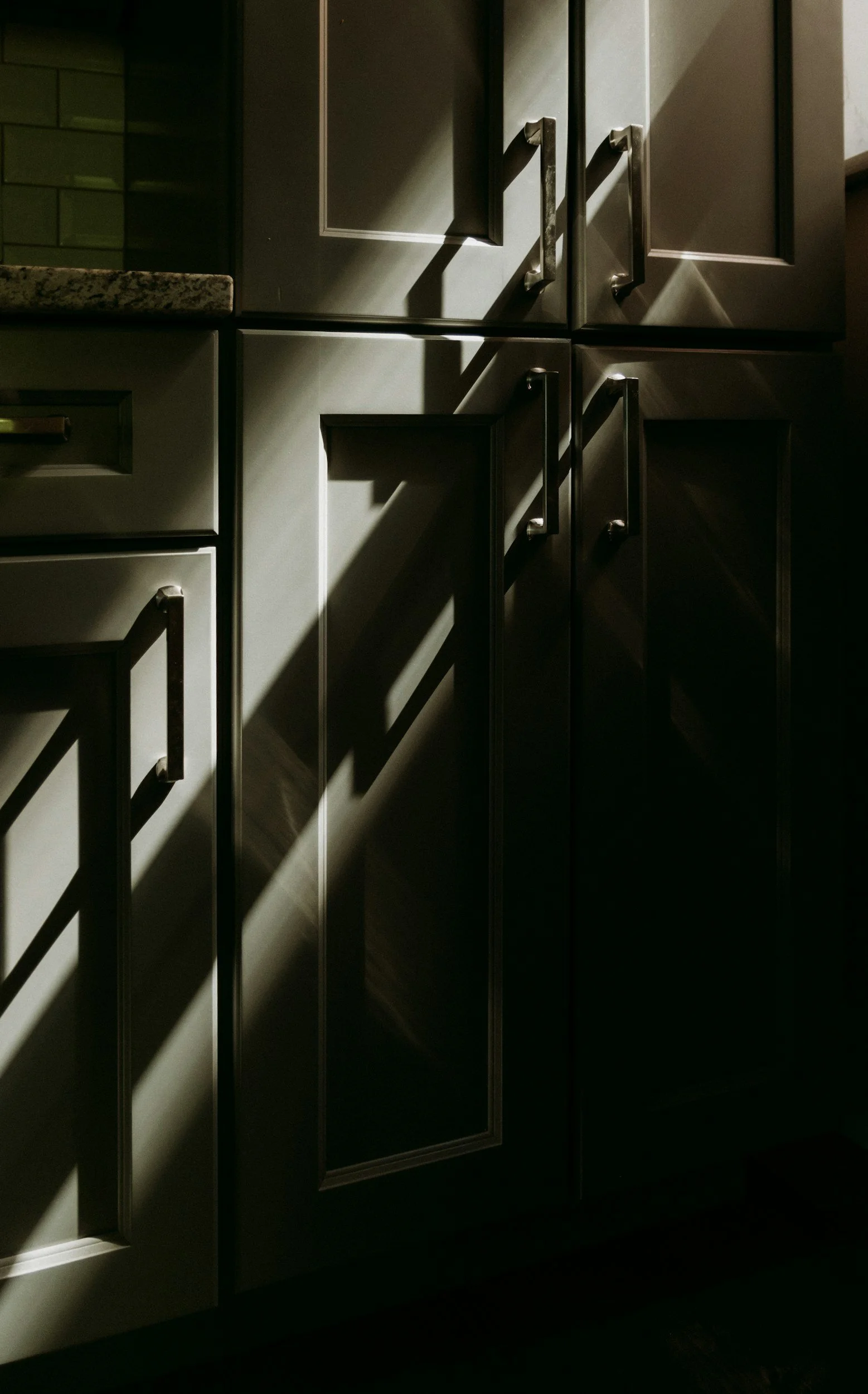 Close-up of kitchen cabinets with sunlight and shadows creating a pattern.
